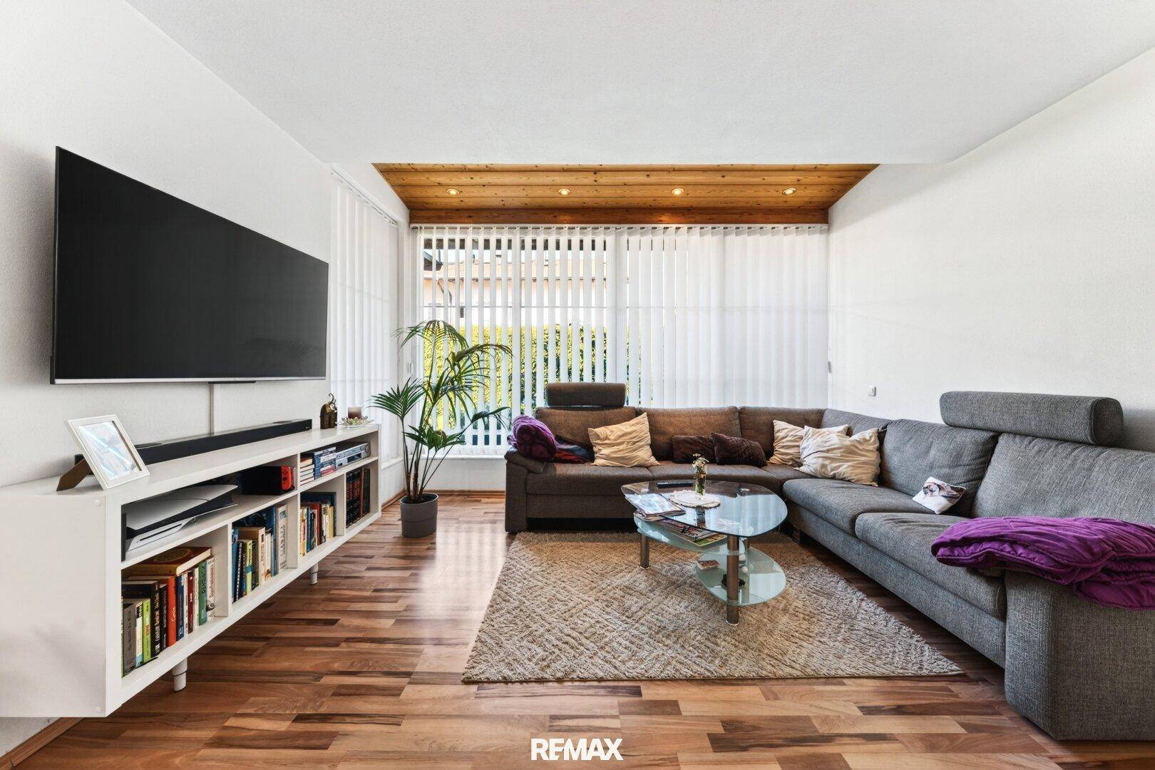 Helles Wohnzimmer mit großem Sofa, Fernseher und Holzboden.