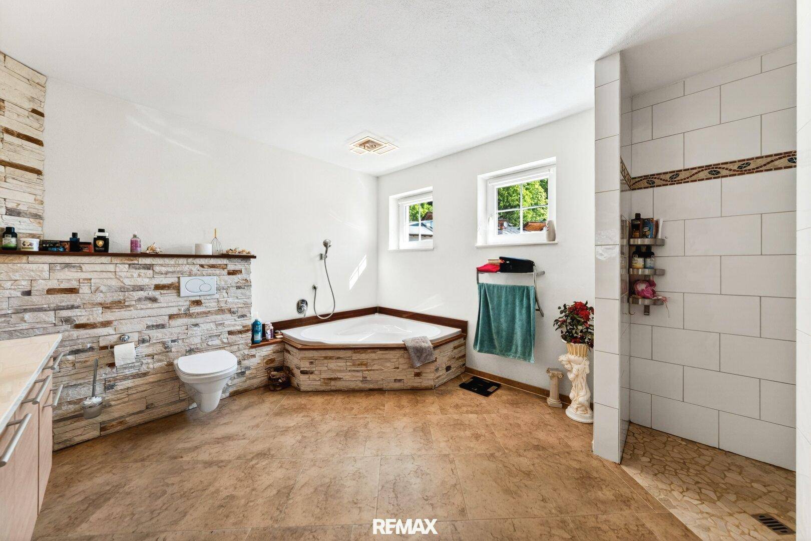 Geräumiges Badezimmer mit Eckbadewanne, Dusche und Steinwand.