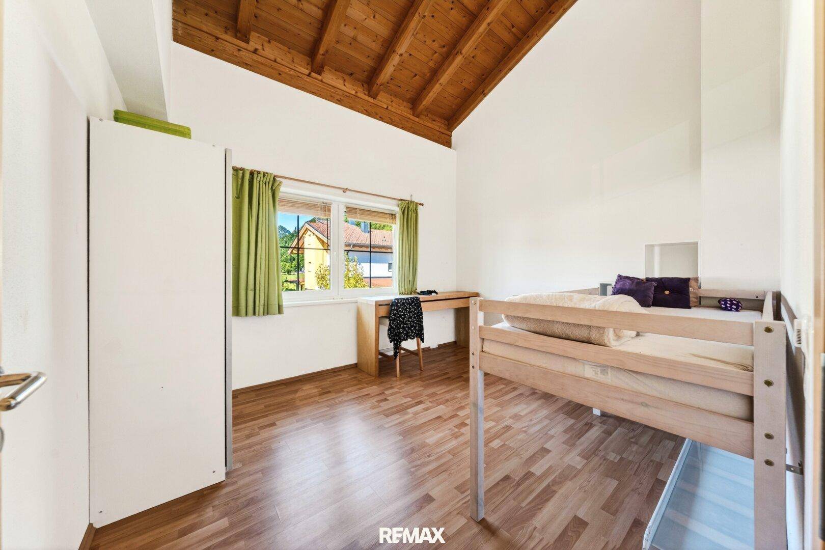 Schlafzimmer mit Holzboden, sichtbaren Dachbalken und hoher Holzdecke, die Gemütlichkeit schafft.