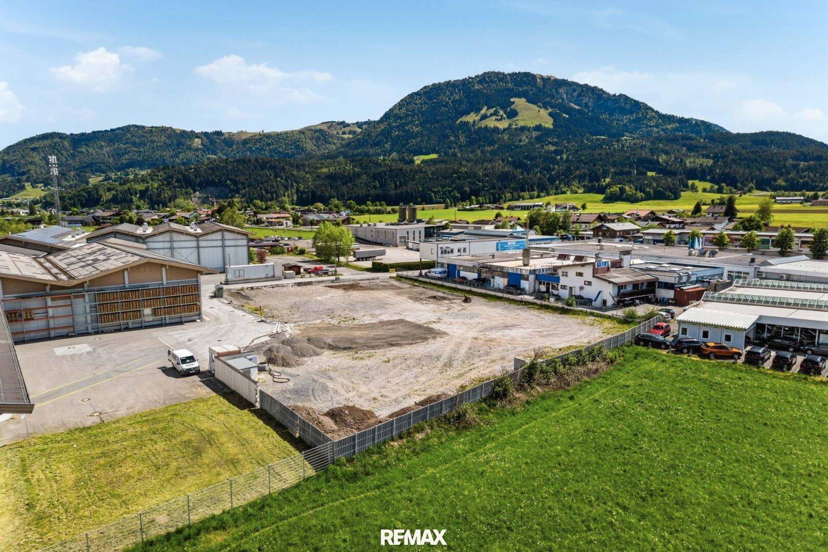 Luftaufnahme eines großen unbebauten Grundstücks in einem Gewerbegebiet, umgeben von bestehenden Hallen und Natur.