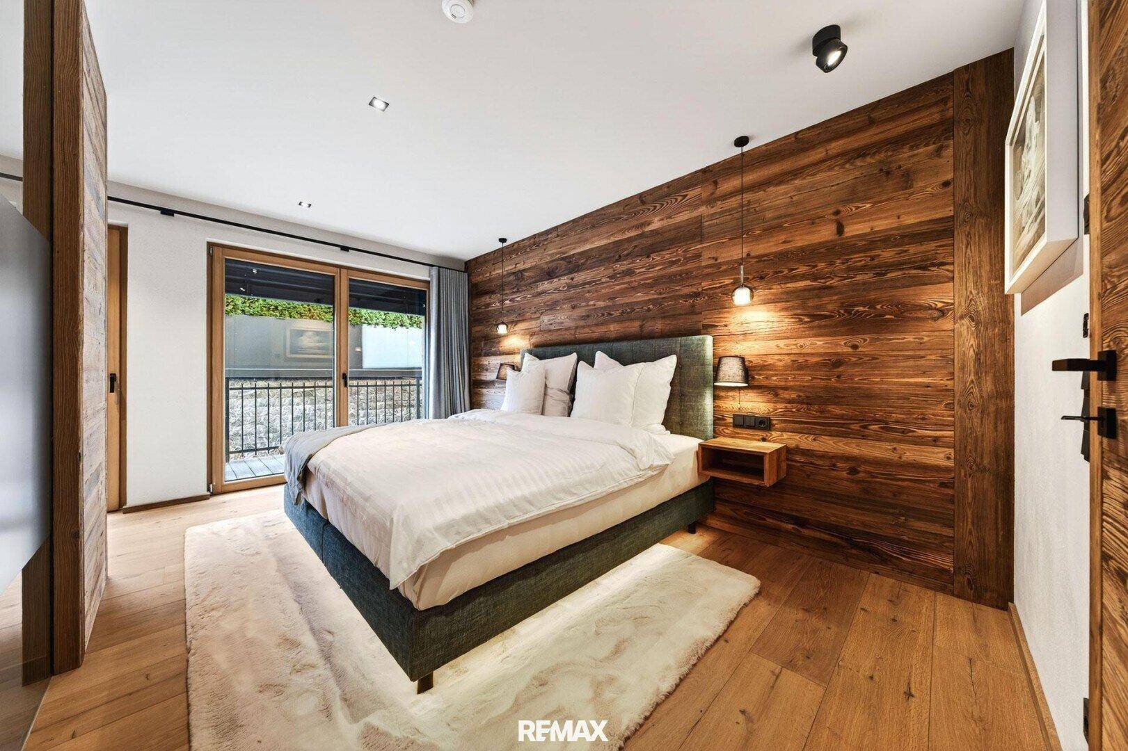 Gemütliches Schlafzimmer mit Holzwand, großem Bett und Zugang zu einem kleinen Balkon.