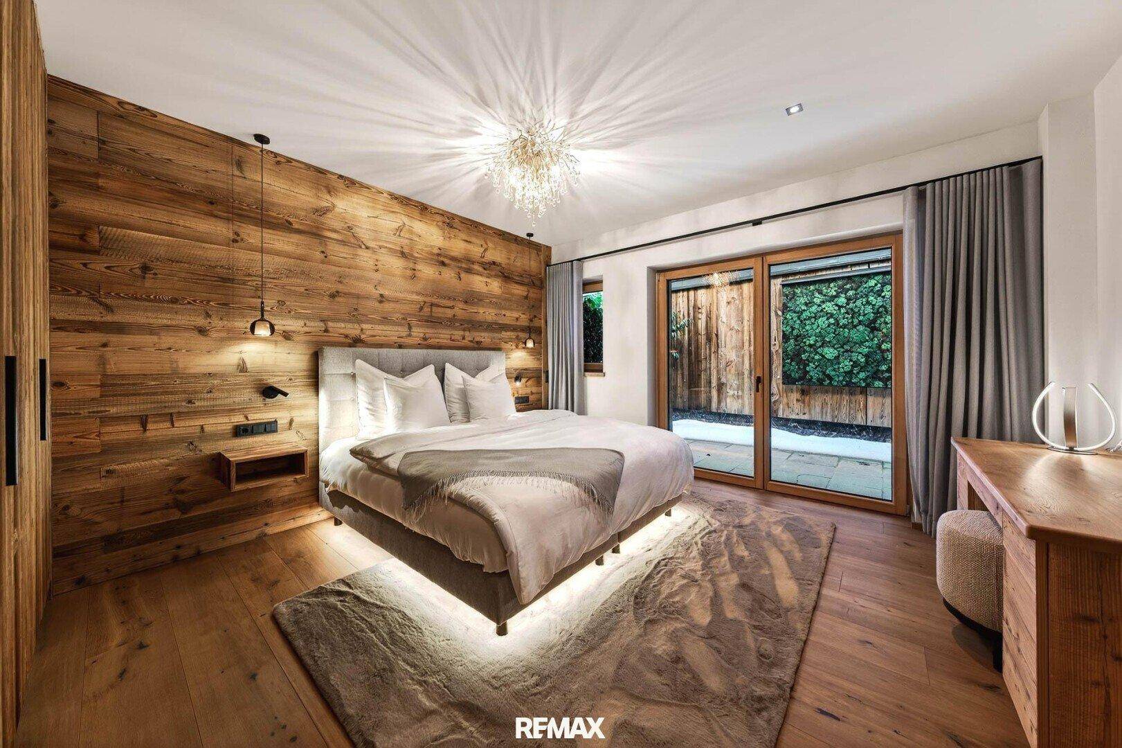 Stilvolles Schlafzimmer mit Holzwand, Parkettboden und großen Fenstern zum Garten.