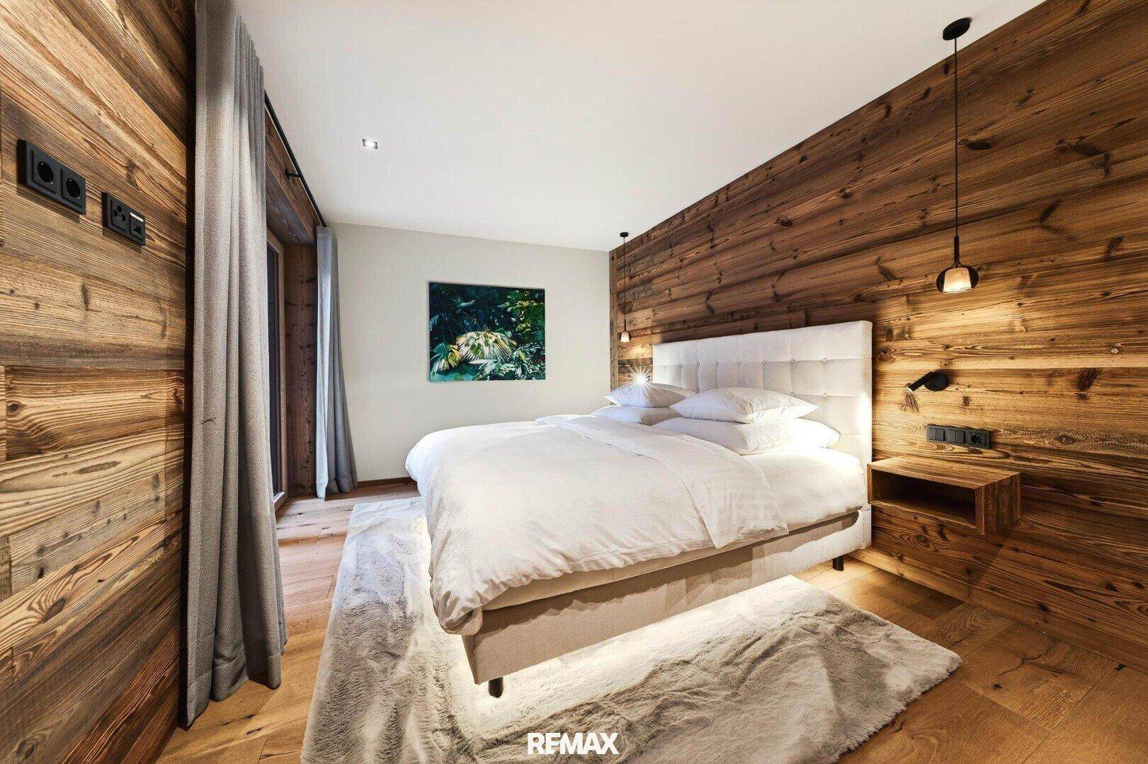 Helles Schlafzimmer mit Holzwand, bequemen Bett und Blick ins Grüne durch das Fenster.
