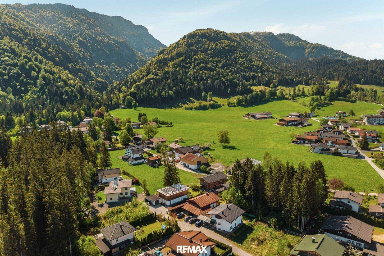 Luftaufnahme eines malerischen Dorfes eingebettet in eine grüne Berglandschaft mit vielen Bäumen.