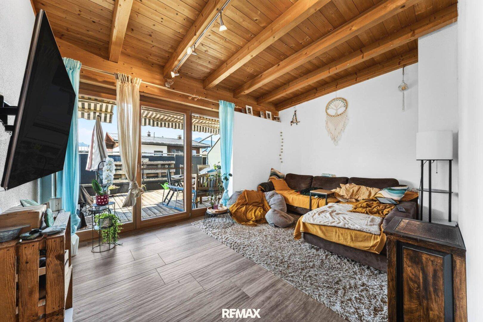 Helles Wohnzimmer mit Holzbalkendecke, Zugang zur Terrasse und gemütlicher Sitzecke.