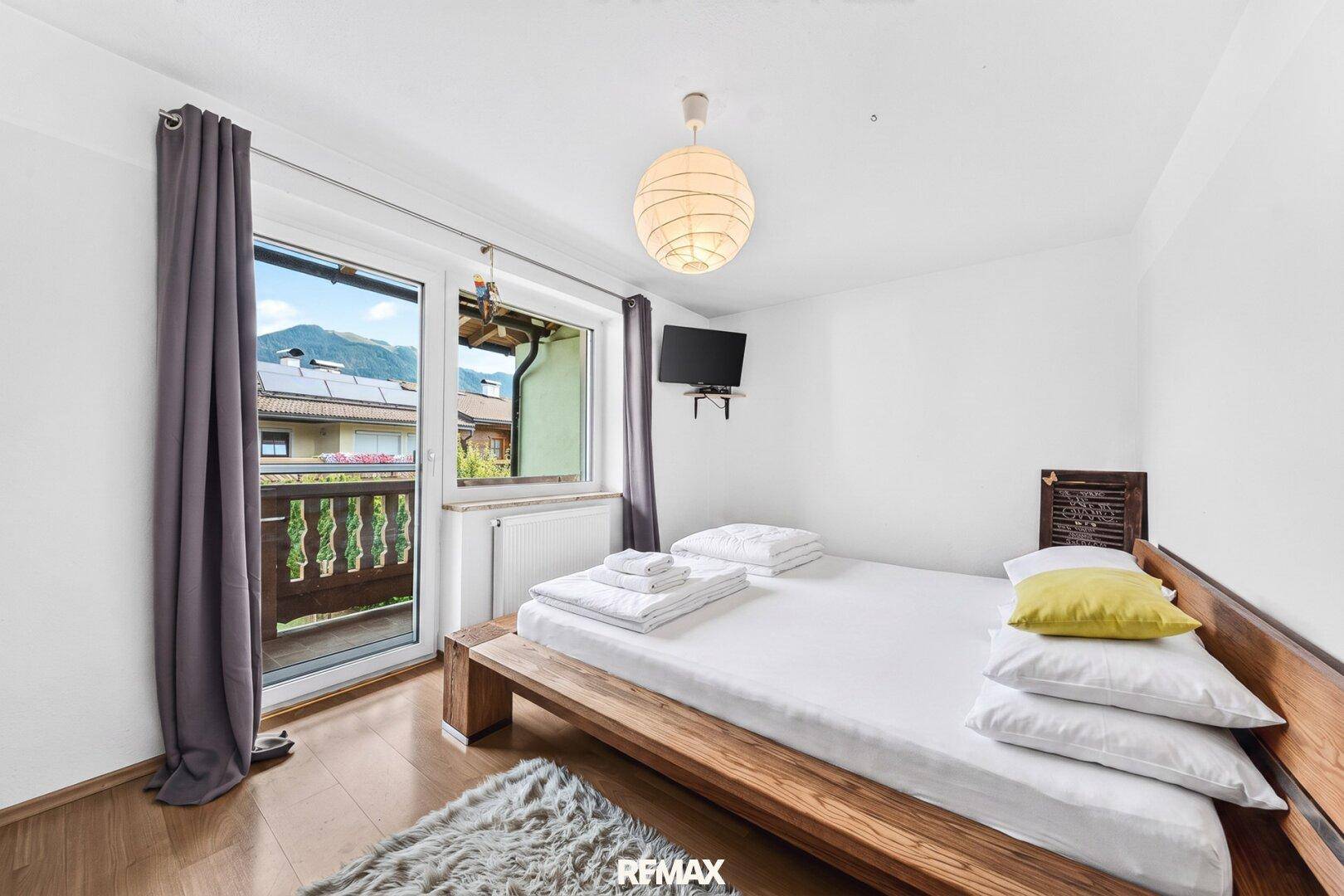 Helles Schlafzimmer mit Holzbett, Balkonzugang und Blick auf die Berge.