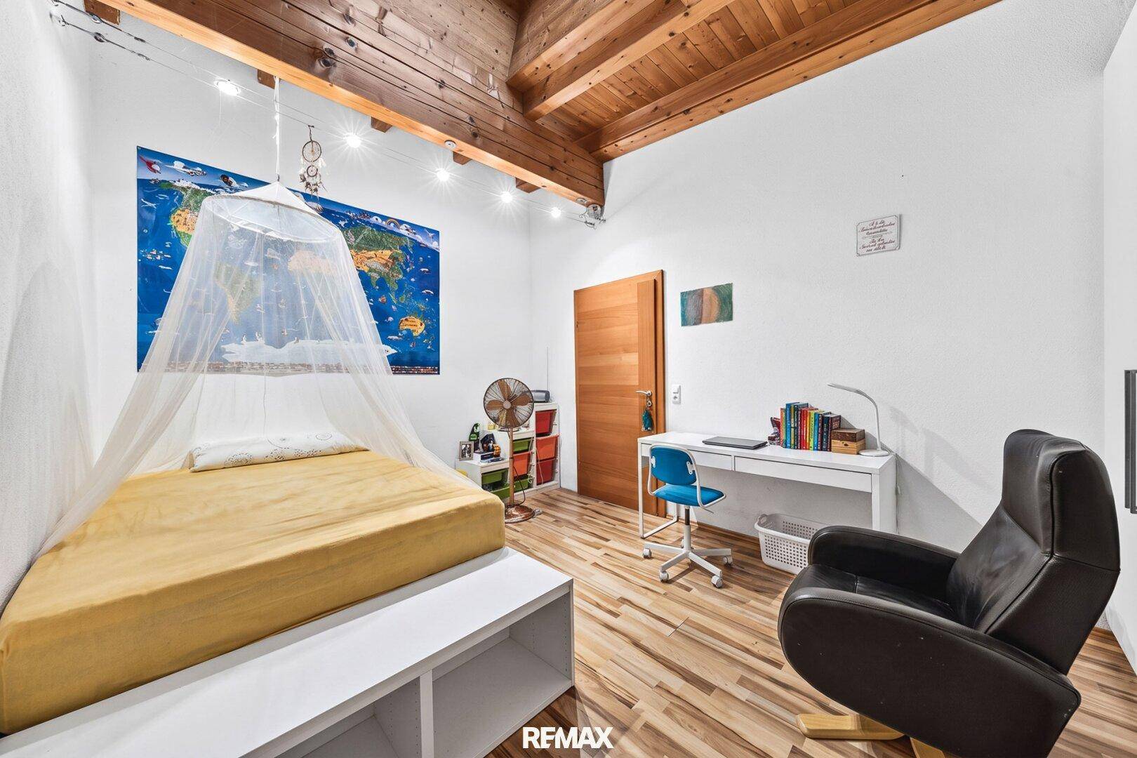 Kinderzimmer mit Holzbalkendecke, Schreibtisch und einem Moskitonetz über dem Bett.