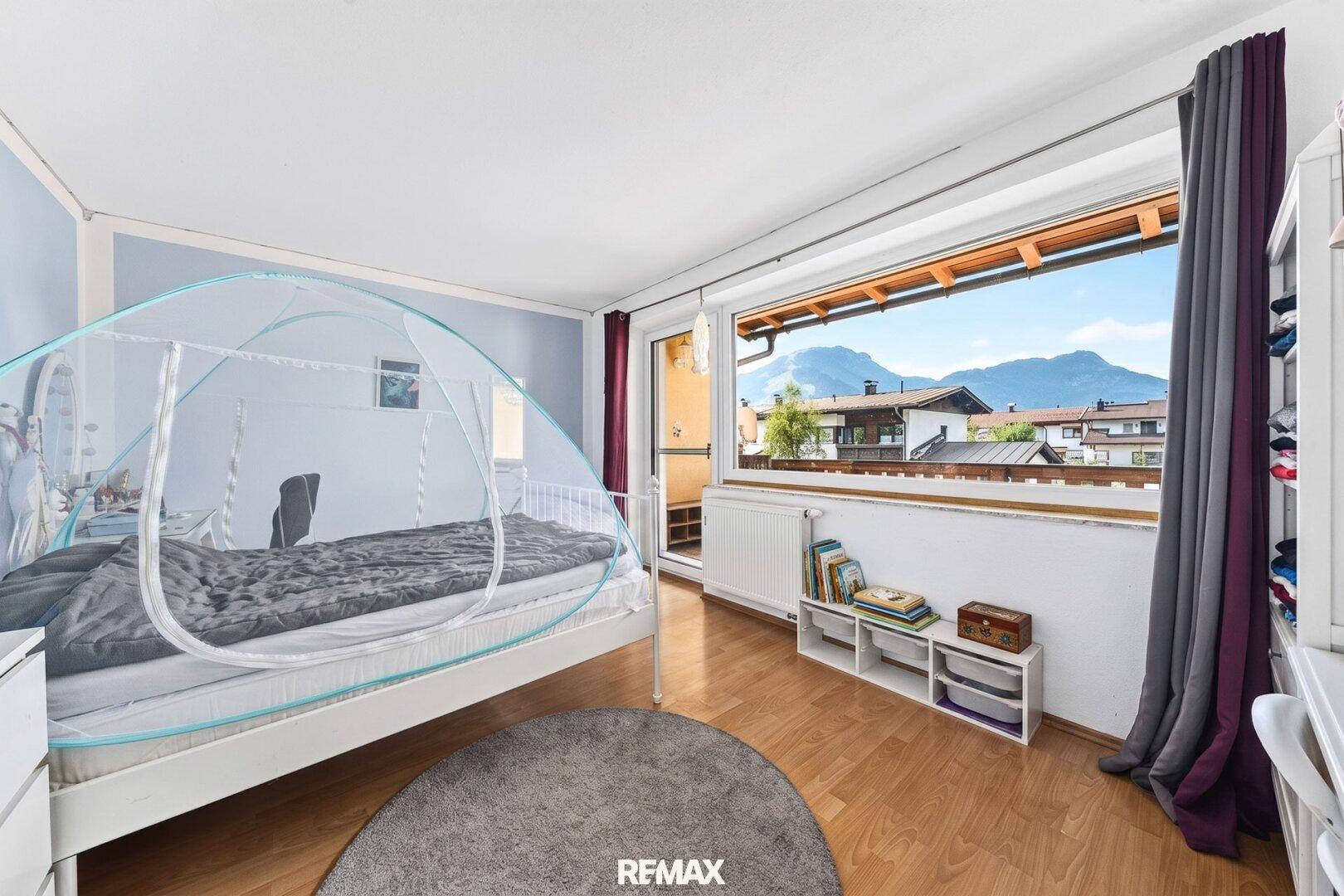 Helles Schlafzimmer mit Bergblick, großem Fenster und Zugang zu einem französischen Balkon.