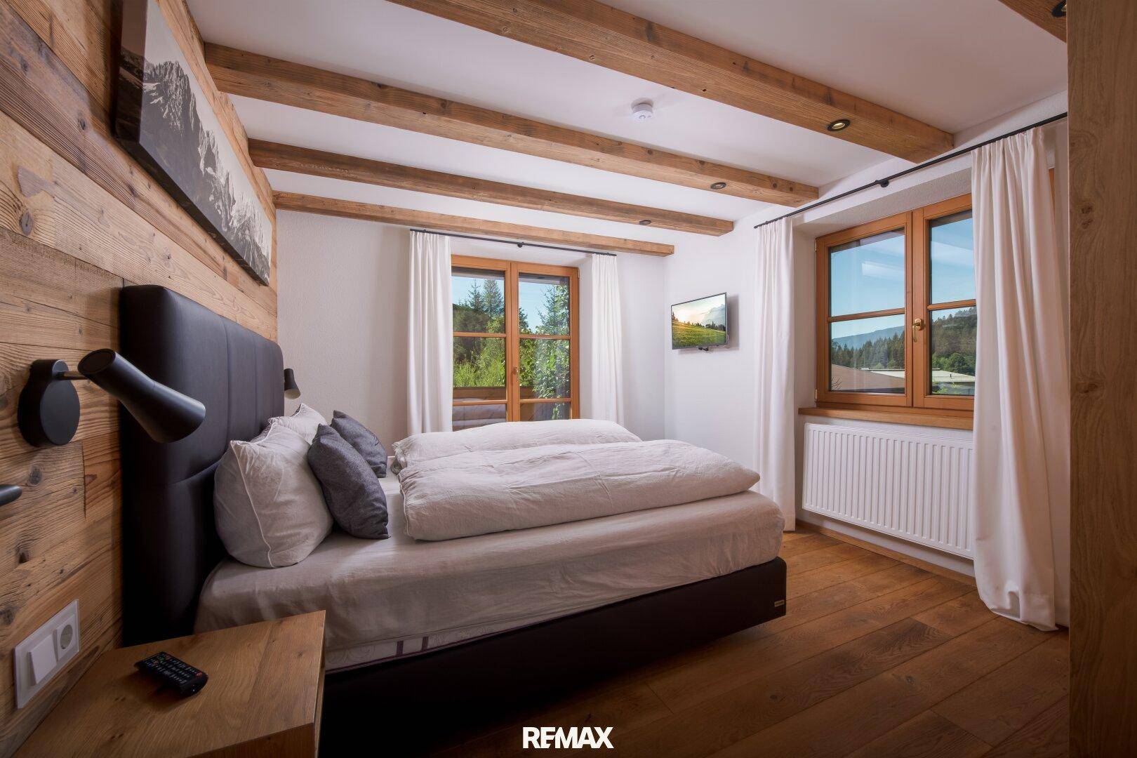 Schlafzimmer im alpinen Stil mit Holzbalken, Holzwänden und Blick auf die umliegende Natur.