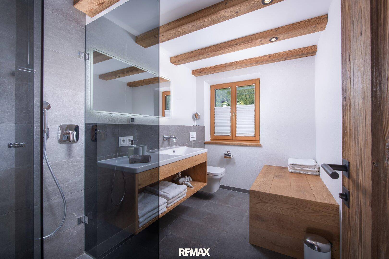 Modernes Badezimmer mit begehbarer Dusche, Holzwaschtisch und grauen Fliesen.