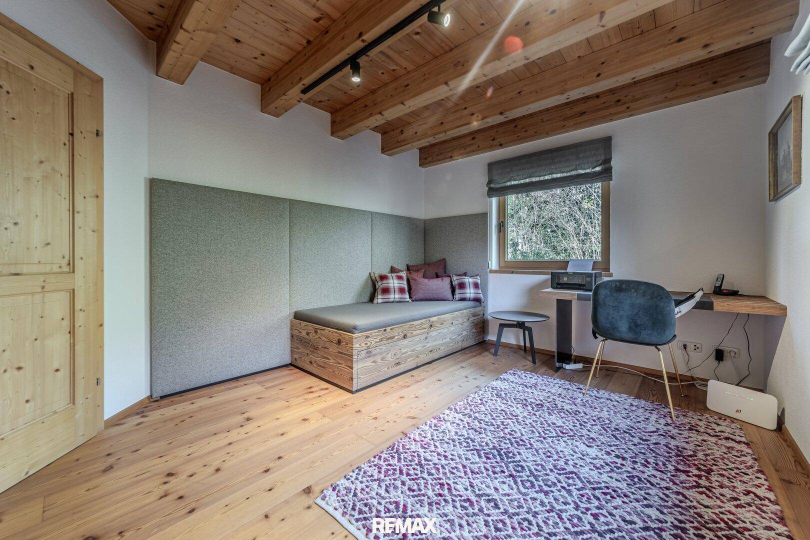 Helles Arbeitszimmer mit Holzboden, Tagesbett und einem Schreibtisch am Fenster.