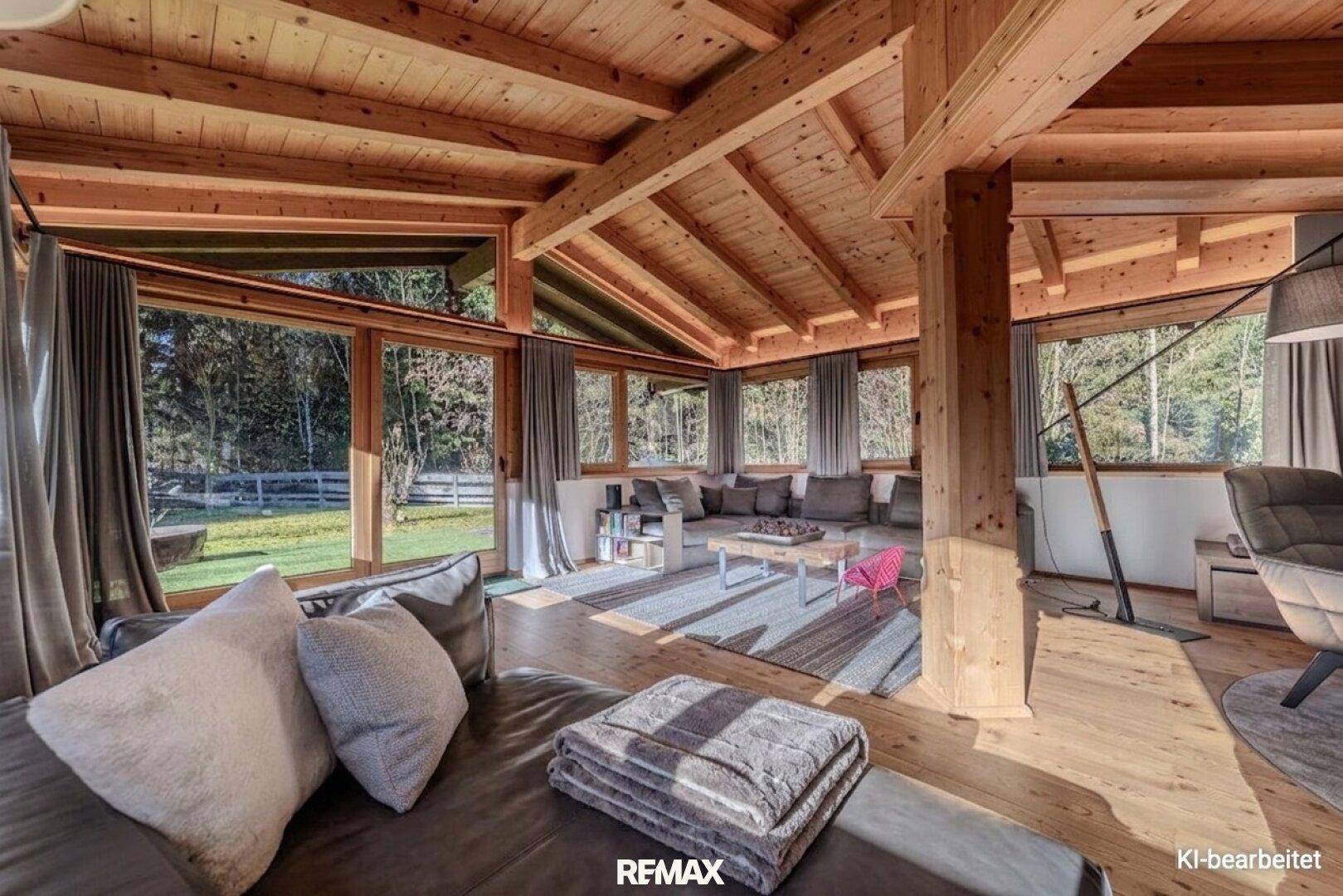 Helles Wohnzimmer mit großen Fenstern, Holzbalkendecke und bequemen Sofas, umgeben von Natur.