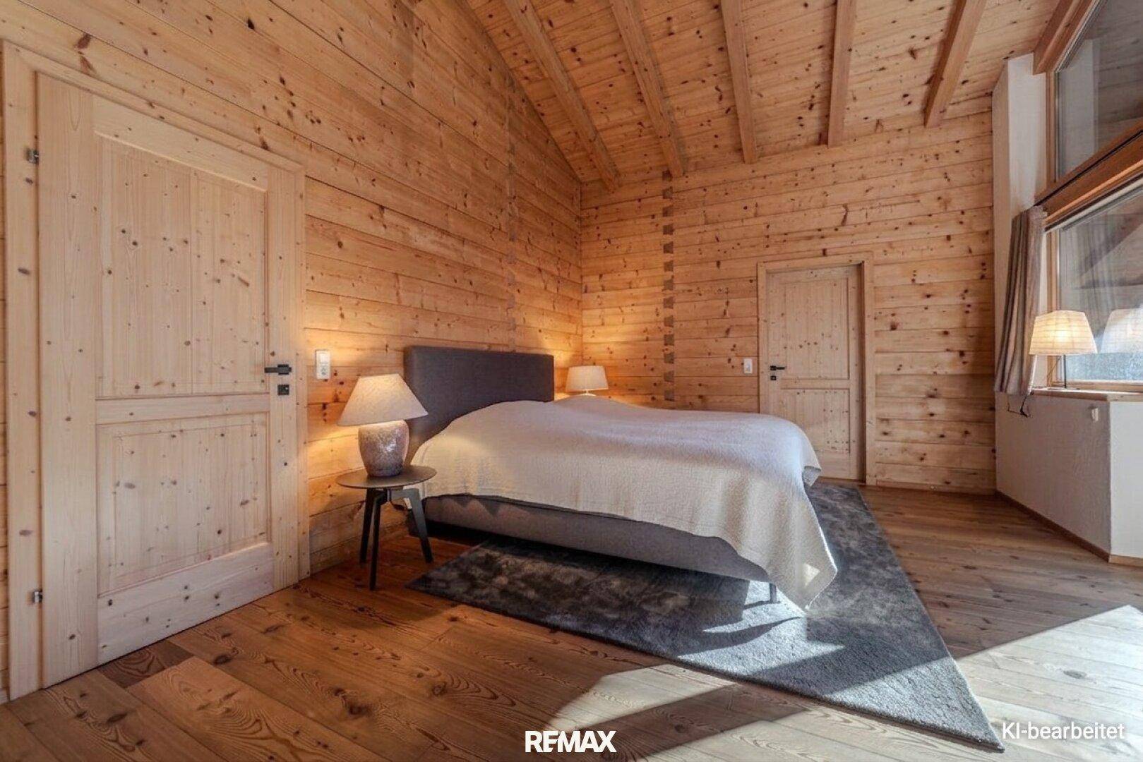 Gemütliches Schlafzimmer mit Holzwänden, Holzbalkendecke und einem großen Bett.
