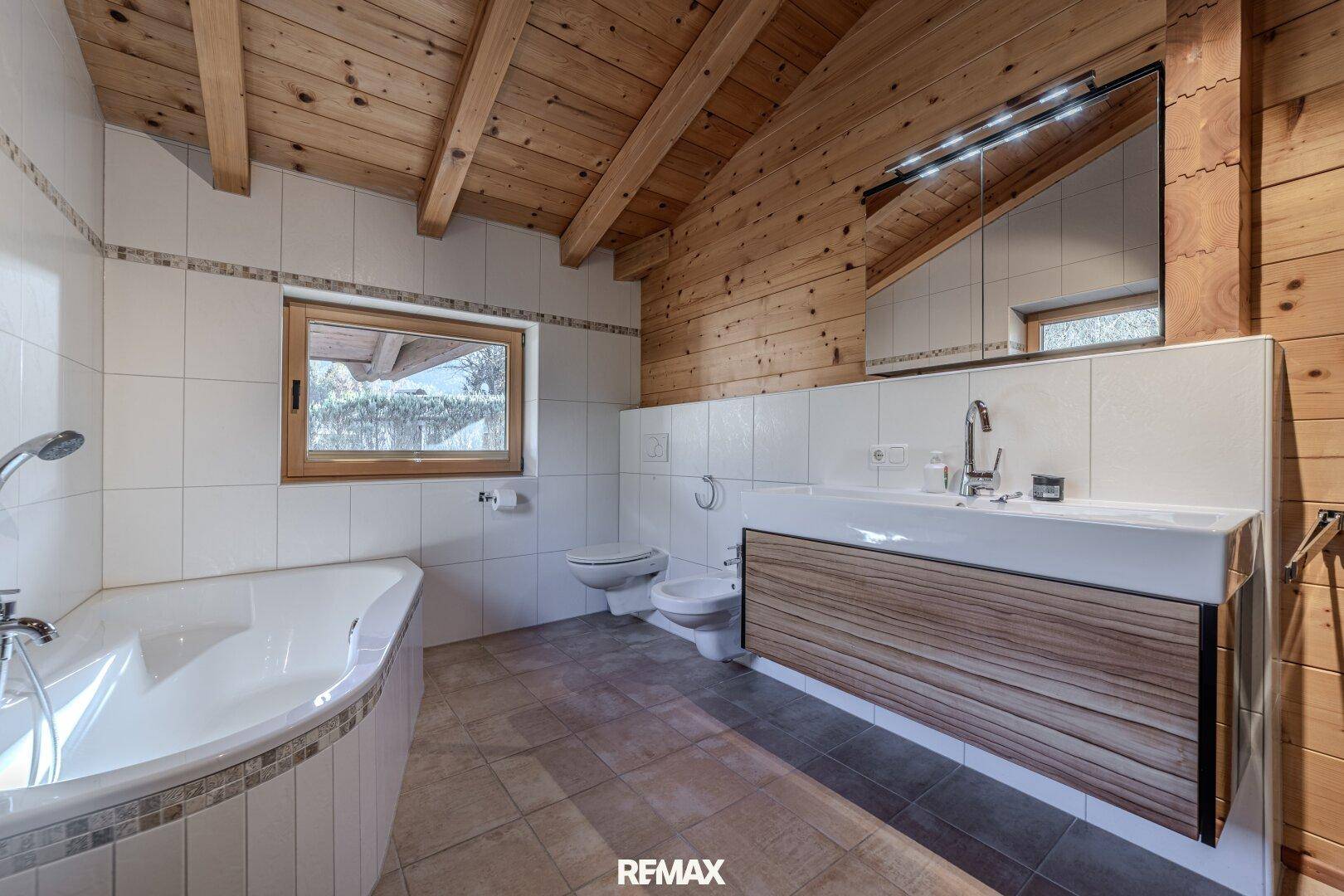 Modernes Badezimmer mit Eckbadewanne, Bidet und großem Waschtisch mit Holzfront.