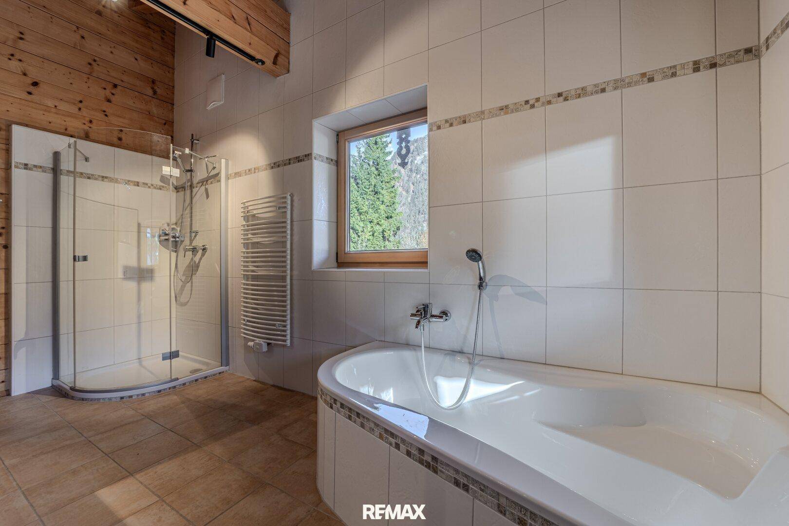 Helles Badezimmer mit Duschkabine, Eckbadewanne und Fenster mit Bergblick.