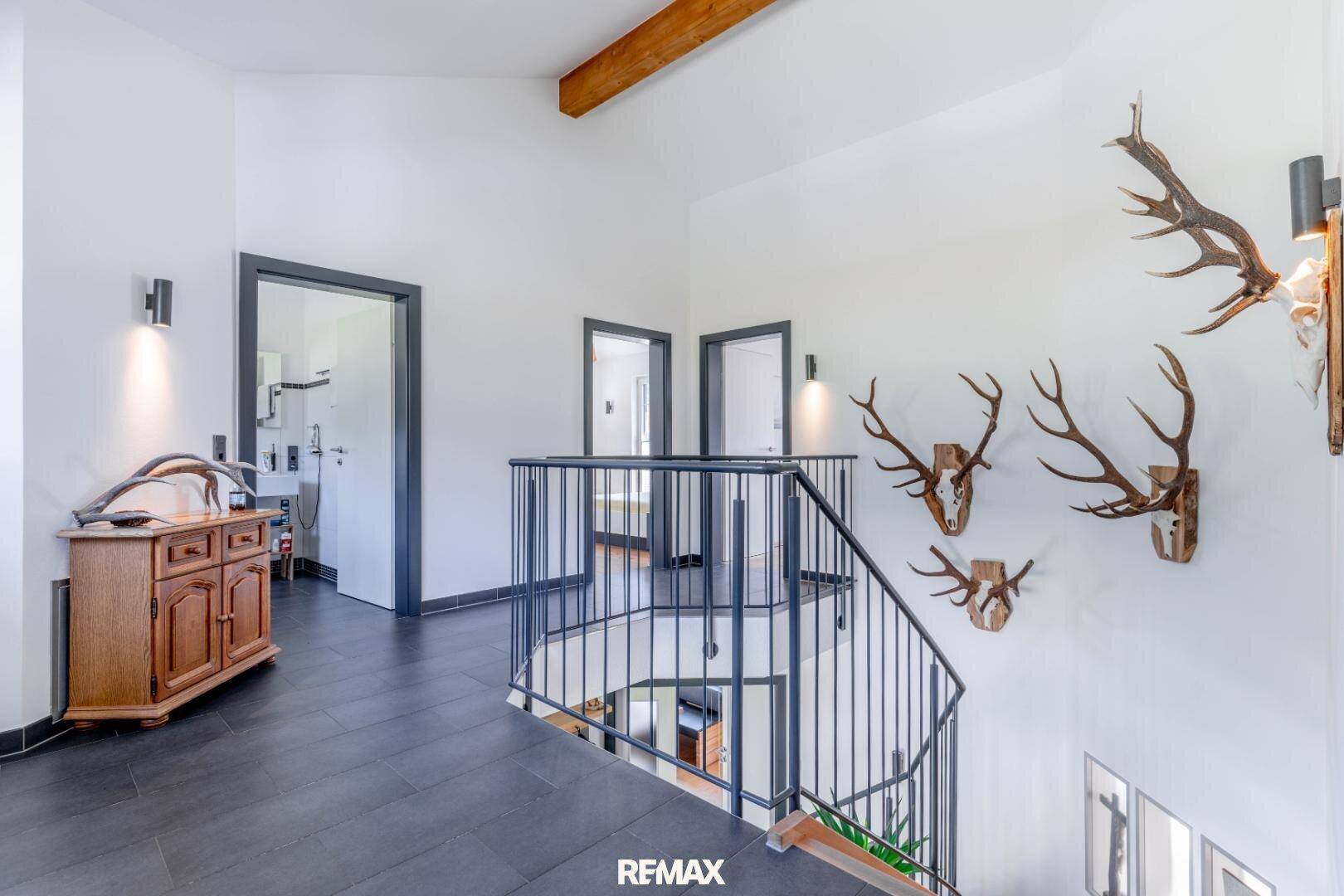 Heller Flur mit dunklen Fliesen, offener Treppe, Holzbalken und traditionellen Geweih-Dekorationen an der Wand.
