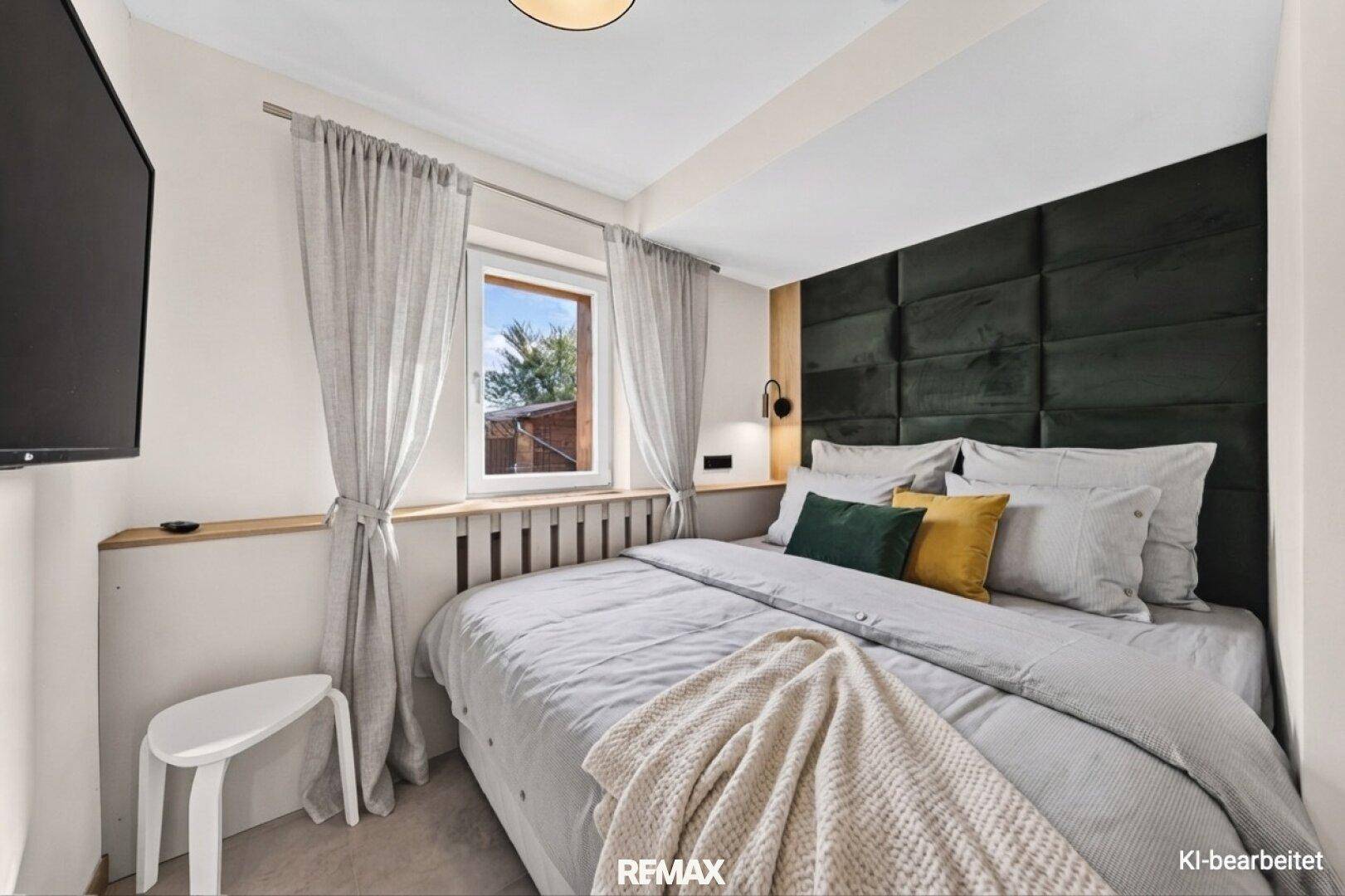 Gemütliches Schlafzimmer mit dunklem Polsterkopfteil und hellem Fenster.