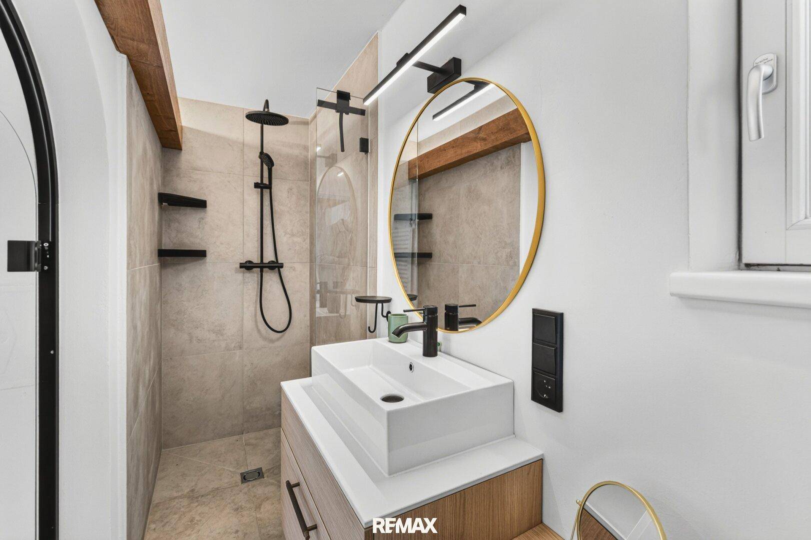 Modernes Badezimmer mit begehbarer Dusche, Aufsatzwaschbecken und goldenem Spiegel.