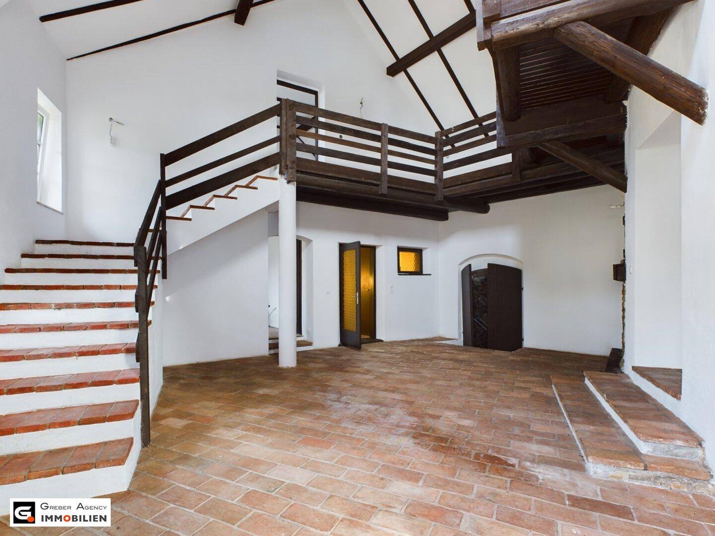 Geräumiger Innenraum mit Terrakottaboden, sichtbaren Holzbalken und einer Holztreppe zur Galerie.