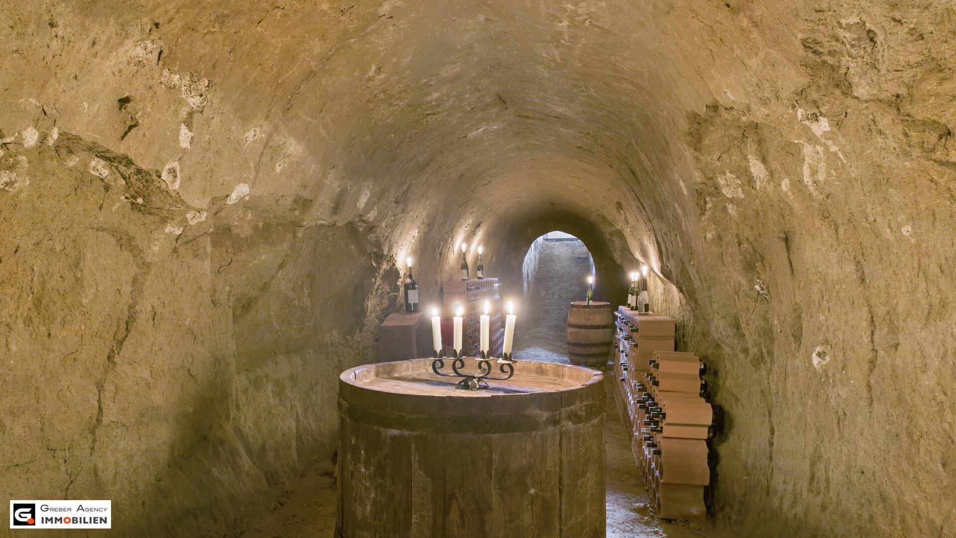 Langer Weinkeller mit gewölbter Decke, gefüllt mit Weinflaschen und beleuchtet von mehreren Kerzen, die den Weg weisen.