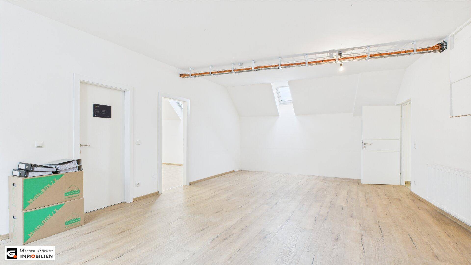 Heller Raum mit Laminatboden, weißen Wänden und einem Dachfenster, das für zusätzliche Belichtung sorgt.