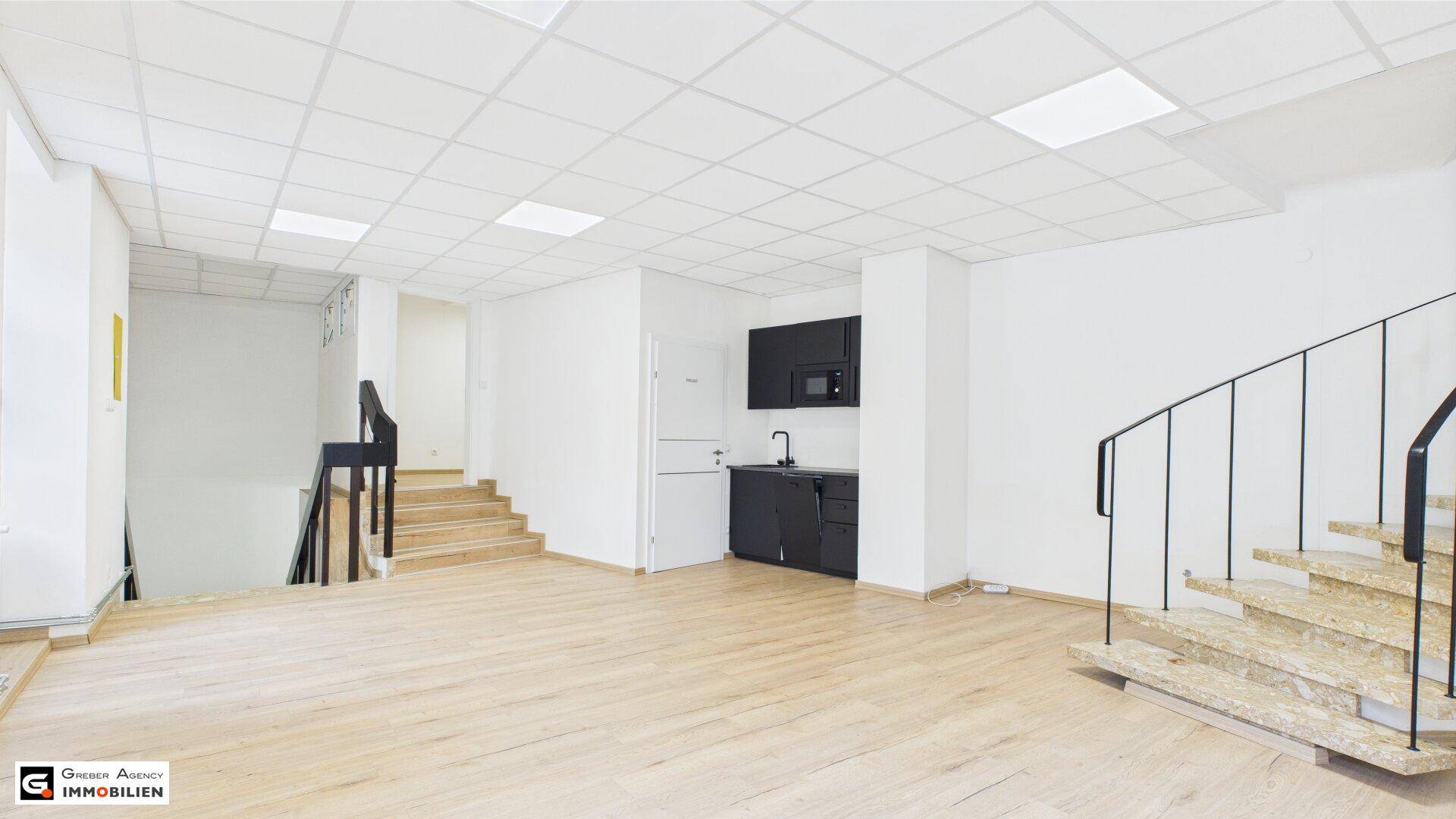 Offener Gewerberaum mit Laminatboden, kleiner Küchenzeile und zwei Treppen, ideal für vielseitige Nutzung.