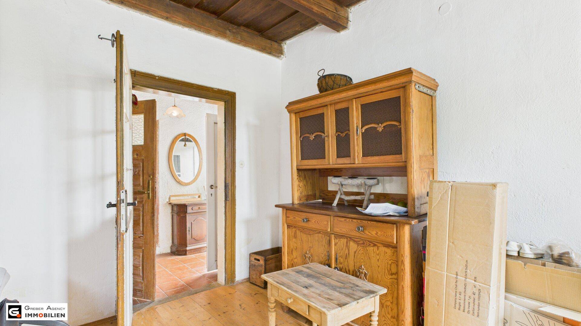 Heller Flur mit Holzbalkendecke und einem traditionellen Holzschrank, der zu weiteren Räumen führt.
