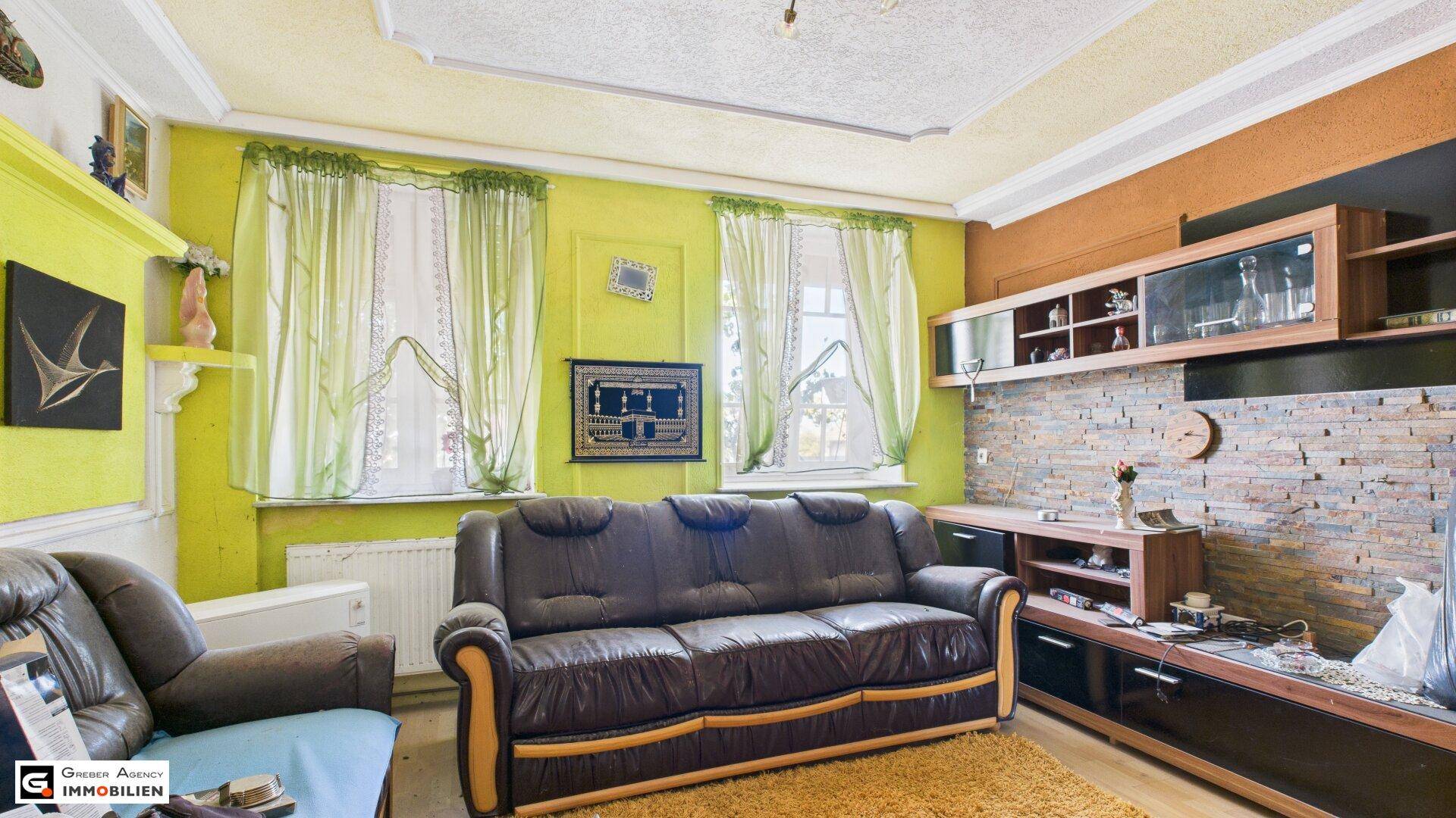 Gemütliches Wohnzimmer mit braunem Ledersofa, gelben Wänden und einer Steinwandverkleidung.