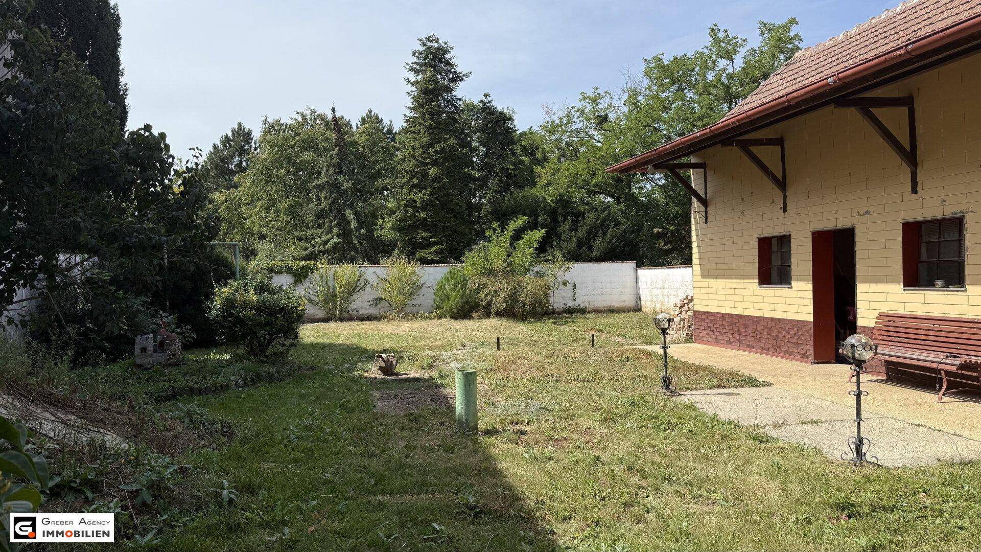 Großer Gartenbereich hinter dem Haus mit Rasenfläche, Bäumen und einer kleinen Terrasse.