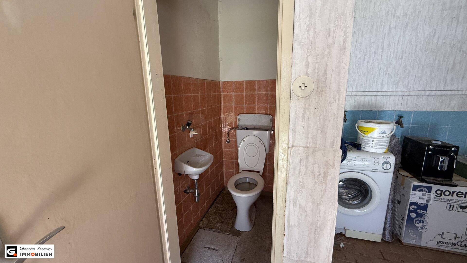 Kleines WC mit Waschbecken, Toilette und orangefarbenen Fliesen im Originalzustand.