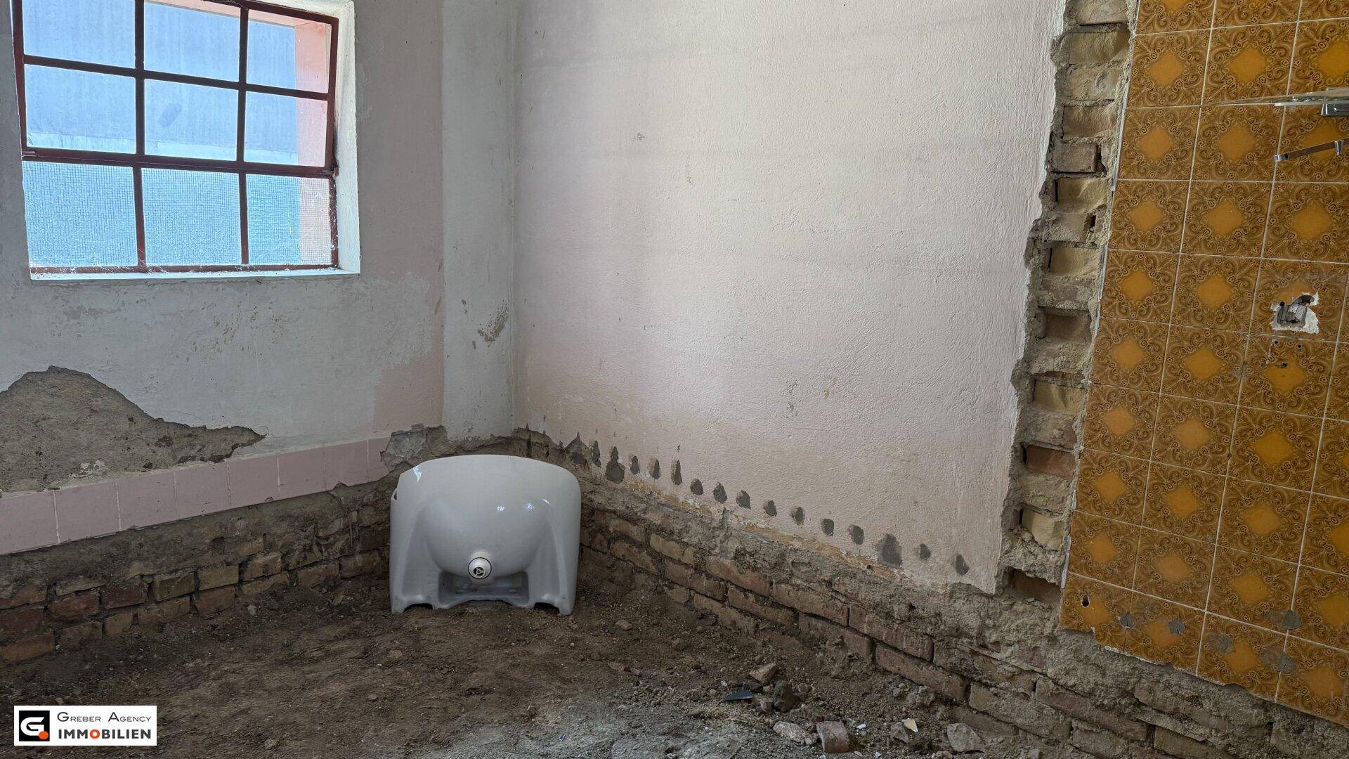 Badezimmer im Rohbau mit freigelegten Wänden und einem Fenster.