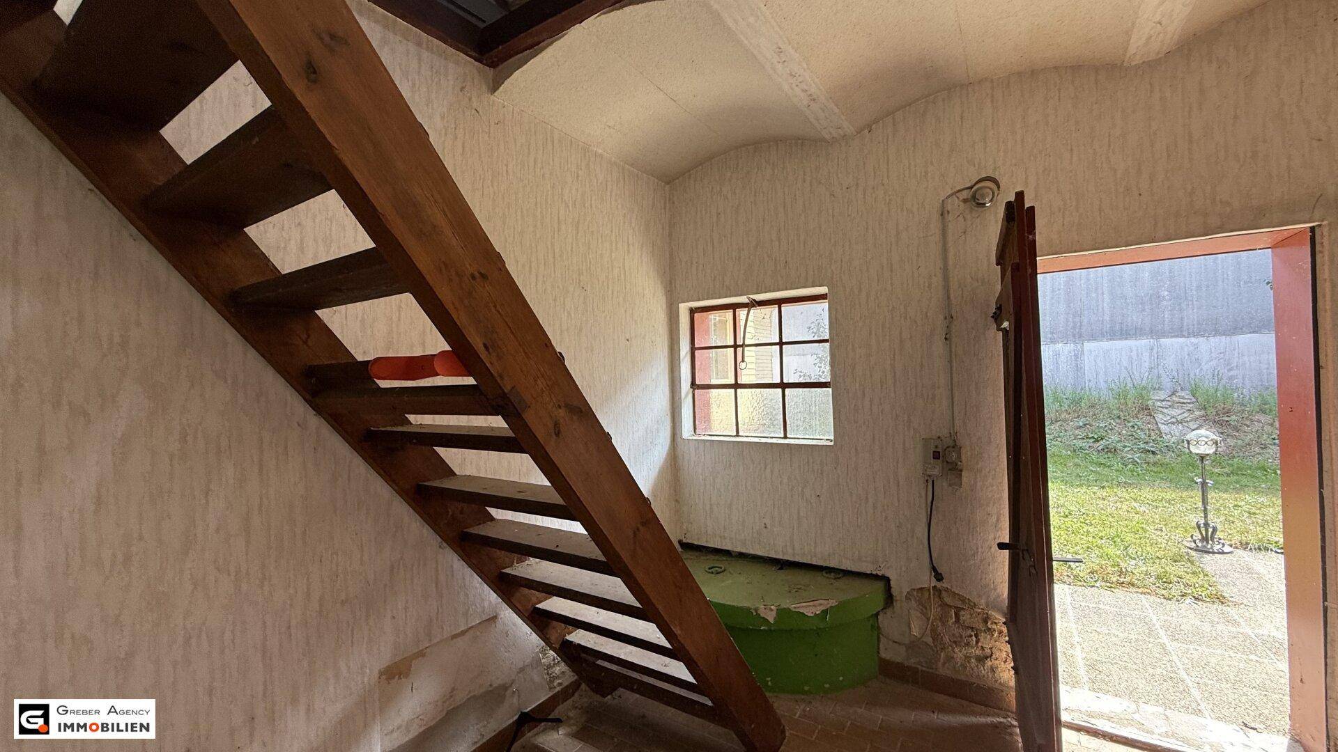 Holztreppe führt in ein Obergeschoss, mit einem Fenster und Zugang zum Garten.