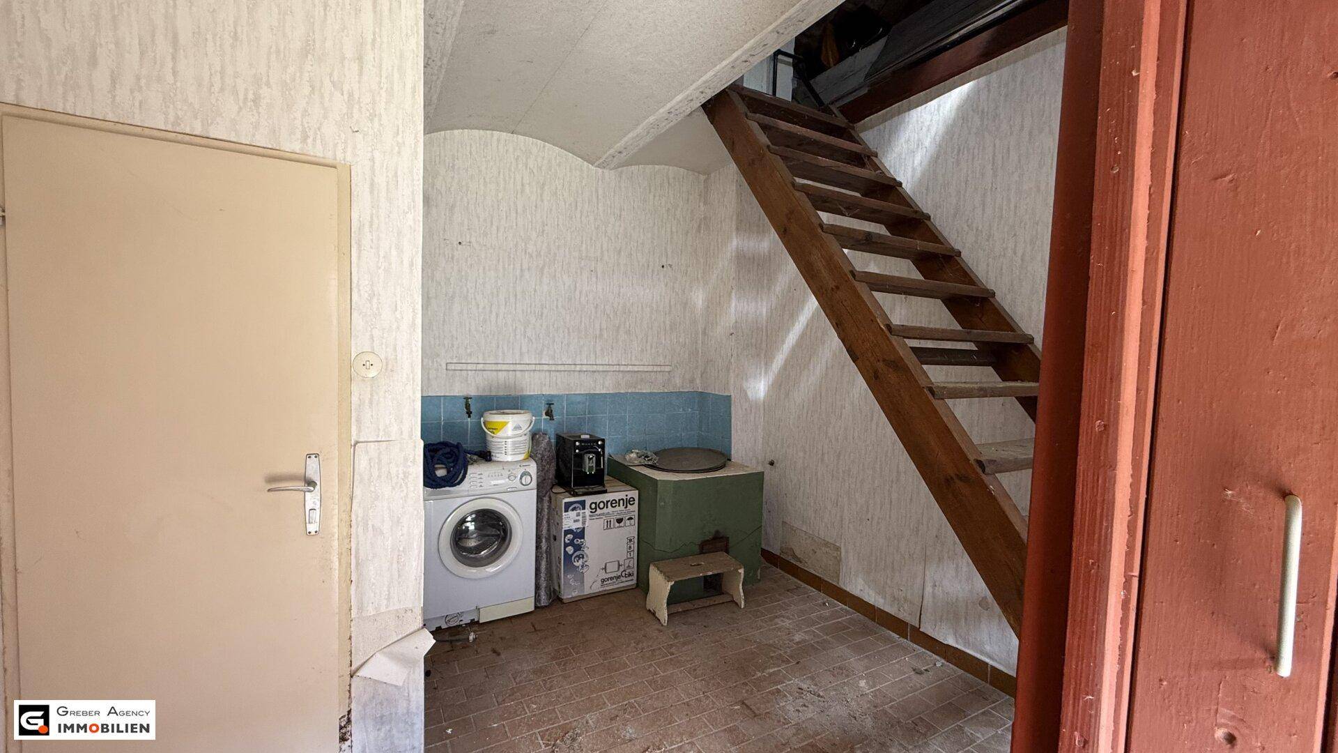 Hauswirtschaftsraum mit Waschmaschine, Spüle und Holztreppe zum Obergeschoss.