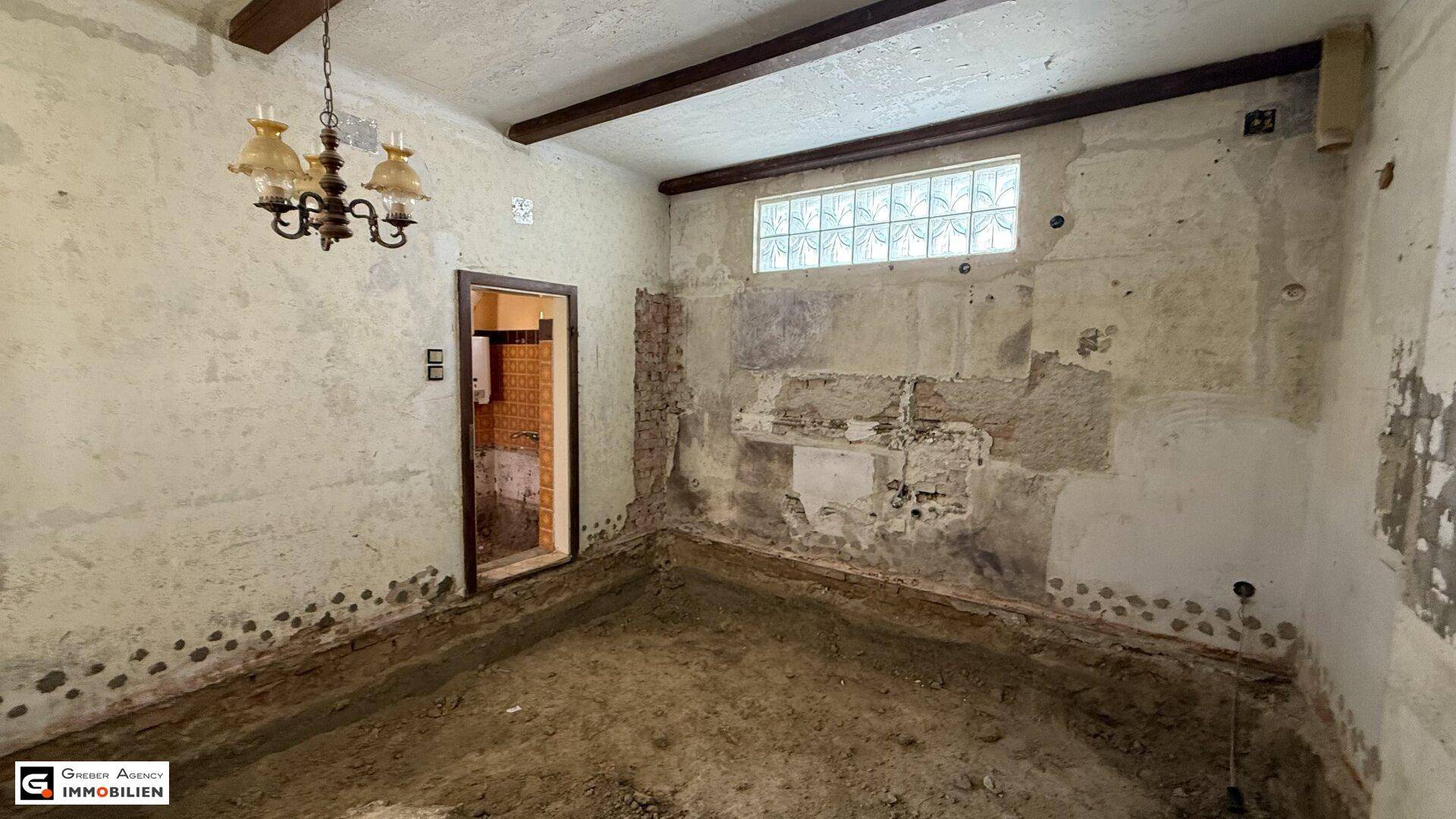 Renovierungsbedürftiger Raum mit freigelegten Wänden, Holzbalken und einem kleinen Fenster.