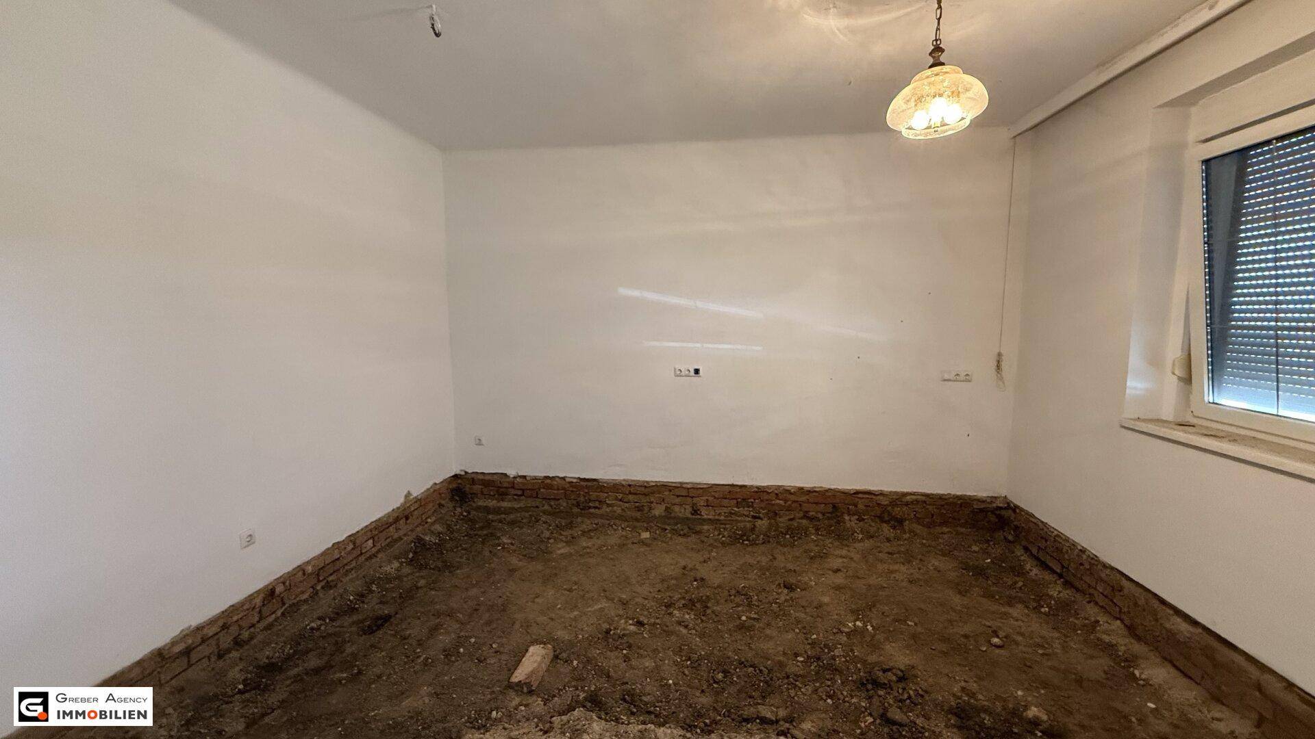 Renovierungsbedürftiger Raum mit weißen Wänden und einem Fenster mit Rollladen.
