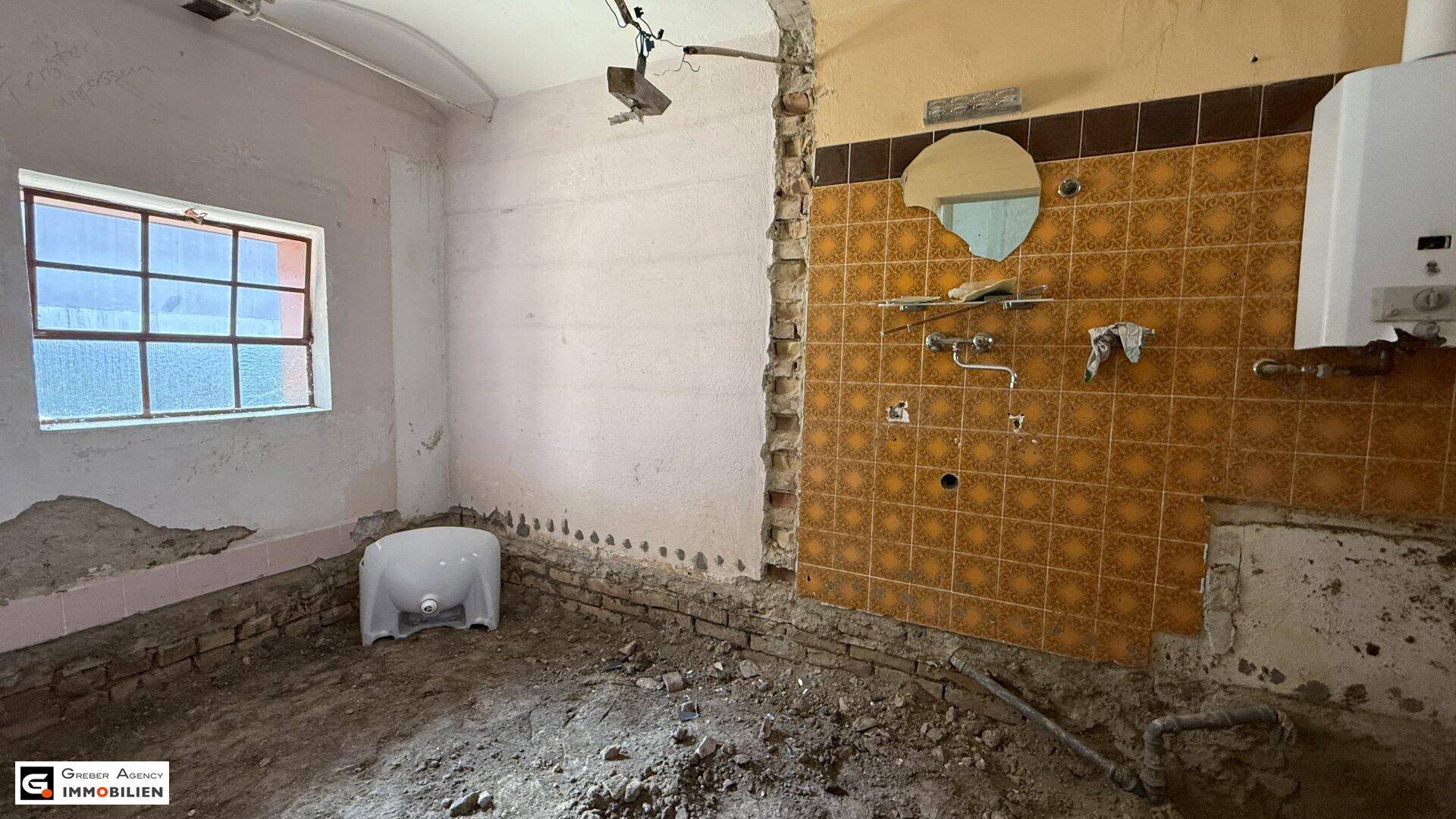 Badezimmer im Rohbau mit alten Fliesen, Gastherme und einem Fenster.