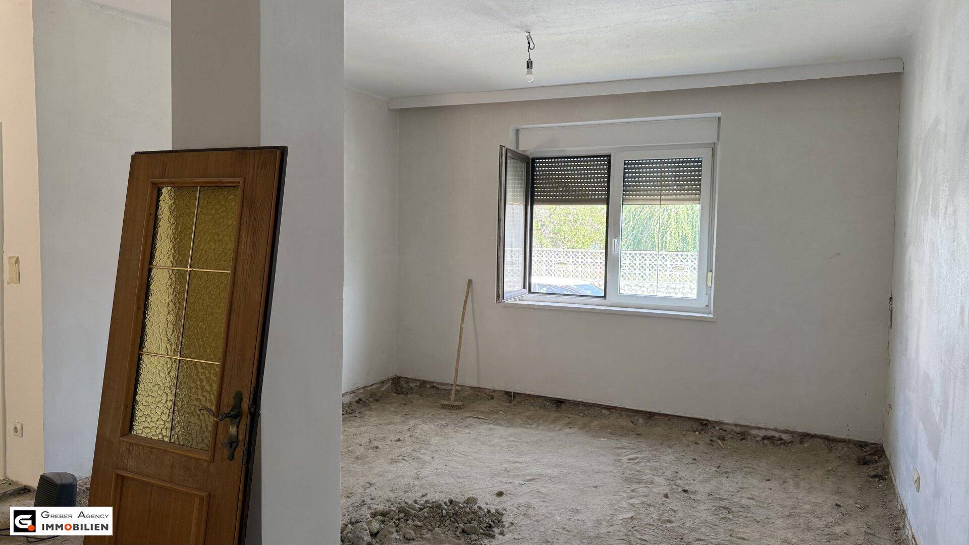Renovierungsbedürftiger Raum mit Fenster, Rollladen und freigelegtem Boden.