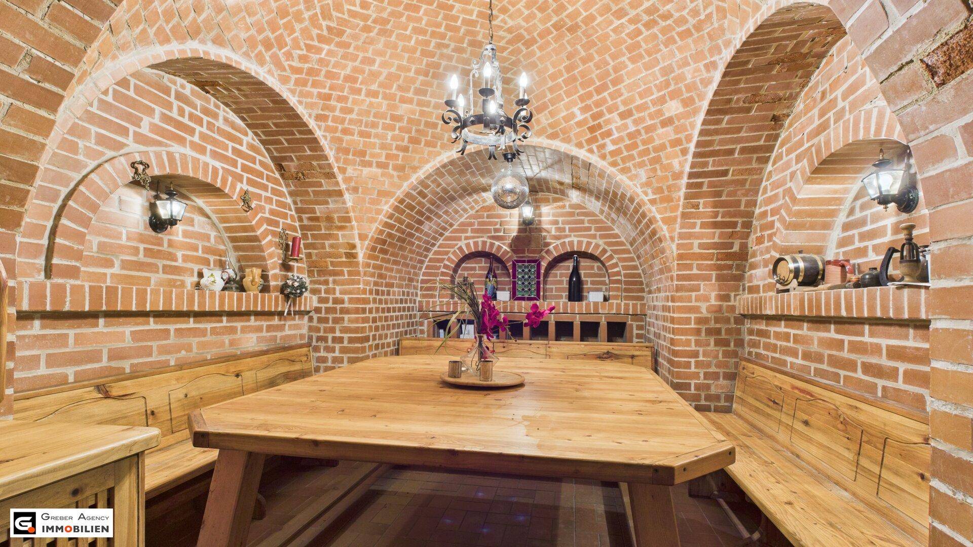 Rustikaler Gewölbekeller mit Ziegelwänden, großem Holztisch und Bänken, ideal für gesellige Runden.