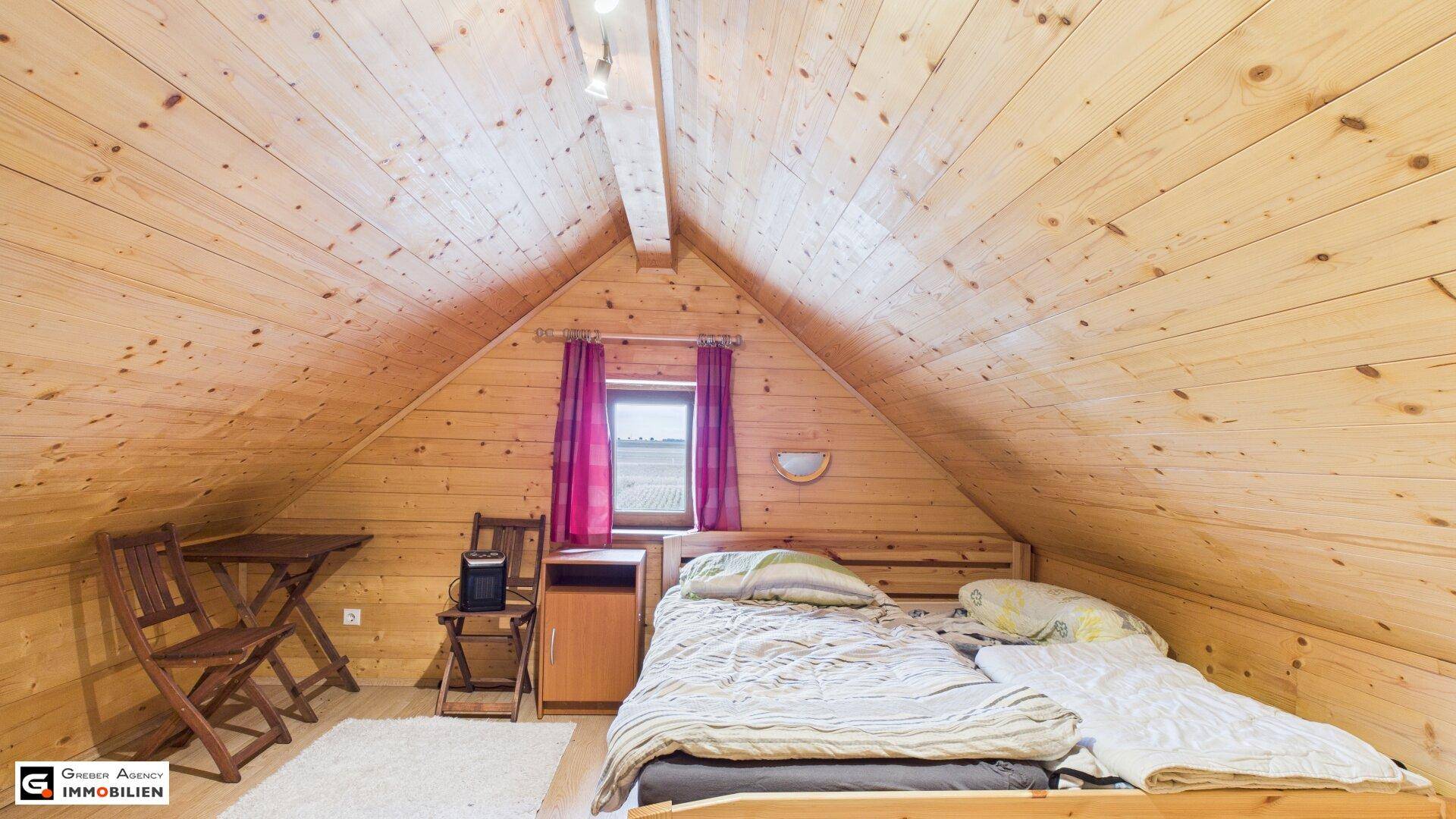Gemütliches Schlafzimmer im Dachgeschoss mit vollständiger Holzverkleidung und Dachschräge.