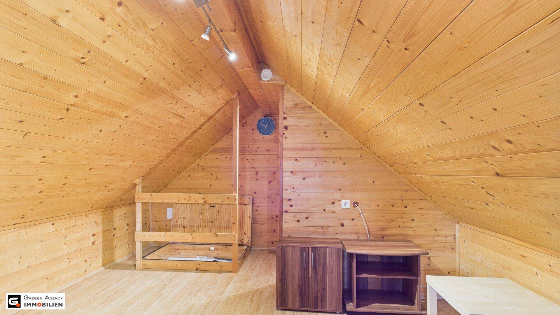 Leerstehender Dachgeschossraum mit Holzverkleidung, Dachschräge und Laminatboden.