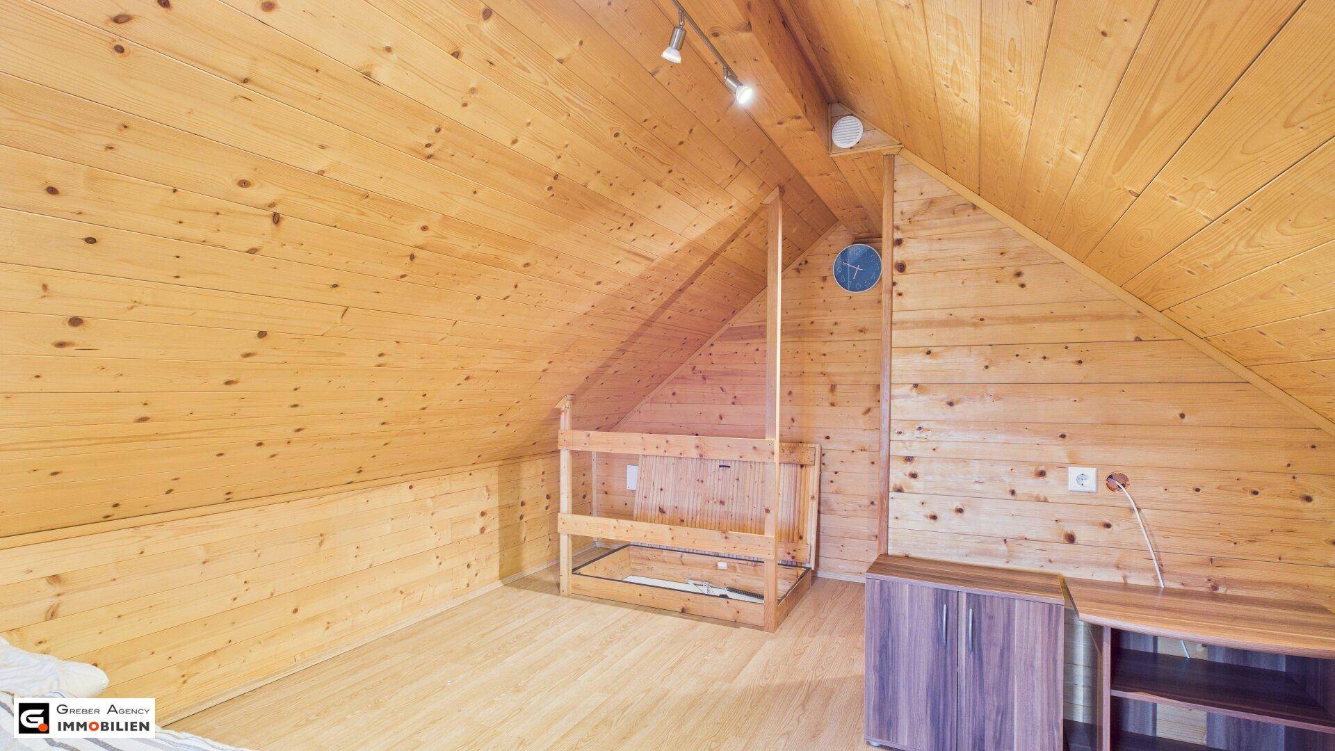 Geräumiger Dachgeschossraum mit Holzverkleidung, Dachschräge und Laminatboden, bereit zur Gestaltung.