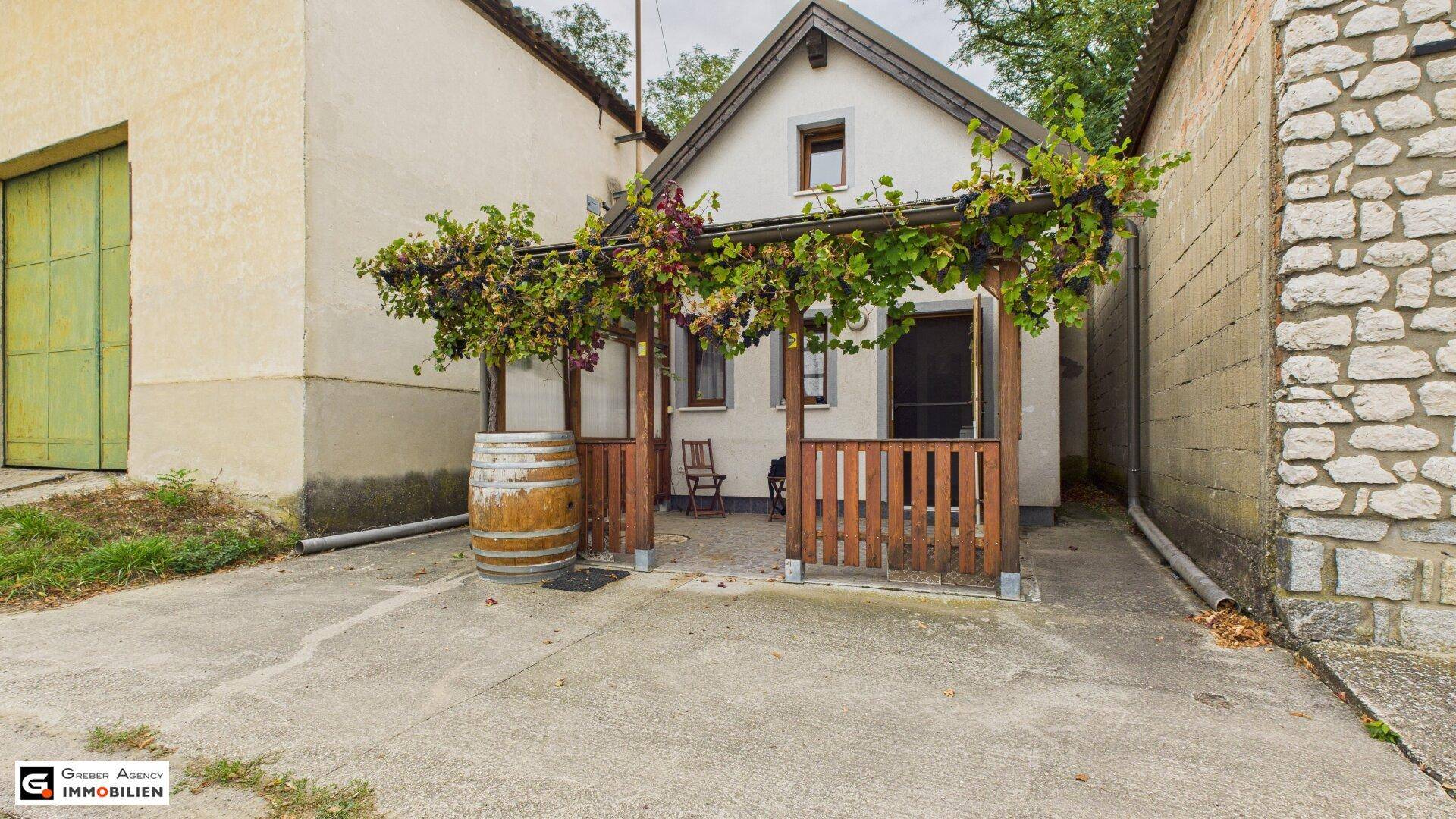 Gesamtansicht des kleinen Hauses mit überdachter Terrasse und umgebender Betonfläche.