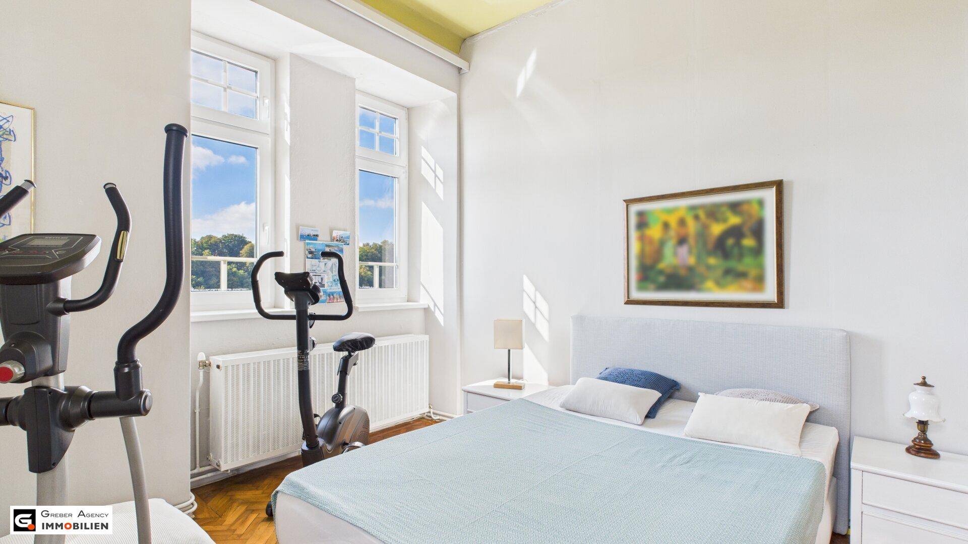 Helles Schlafzimmer mit Holzboden, Sportgeräten und großen Fenstern mit Ausblick.