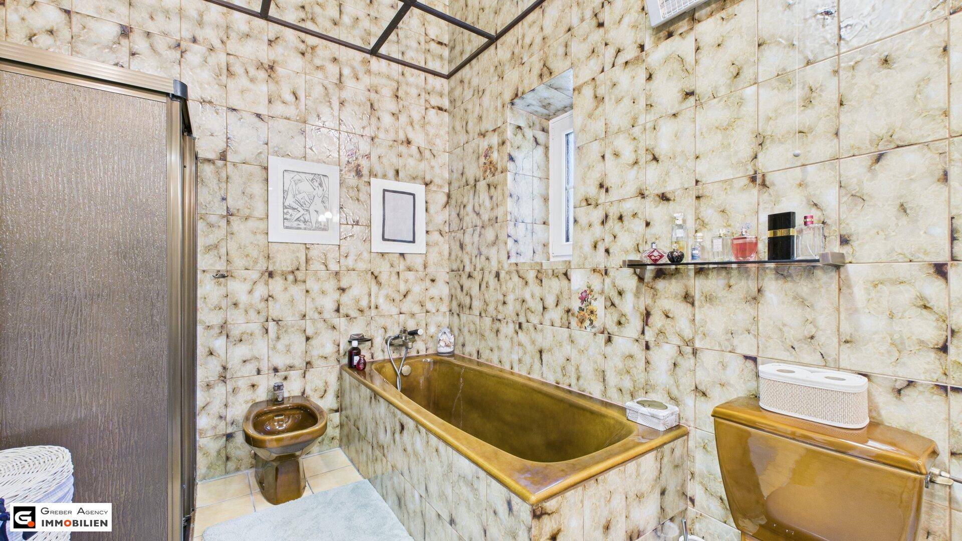 Badezimmer im 80er-Jahre-Stil mit Badewanne, Bidet und gemusterten Fliesen.