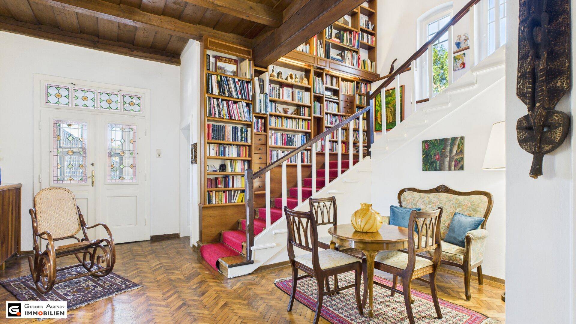 Eingangsbereich mit Holztreppe, eingebautem Bücherregal und Buntglasfenstern.