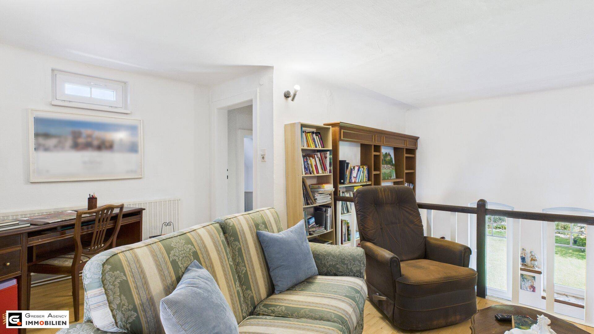 Gemütlicher Wohnbereich im Obergeschoss mit Sofa, Bücherregal und Blick ins Grüne.