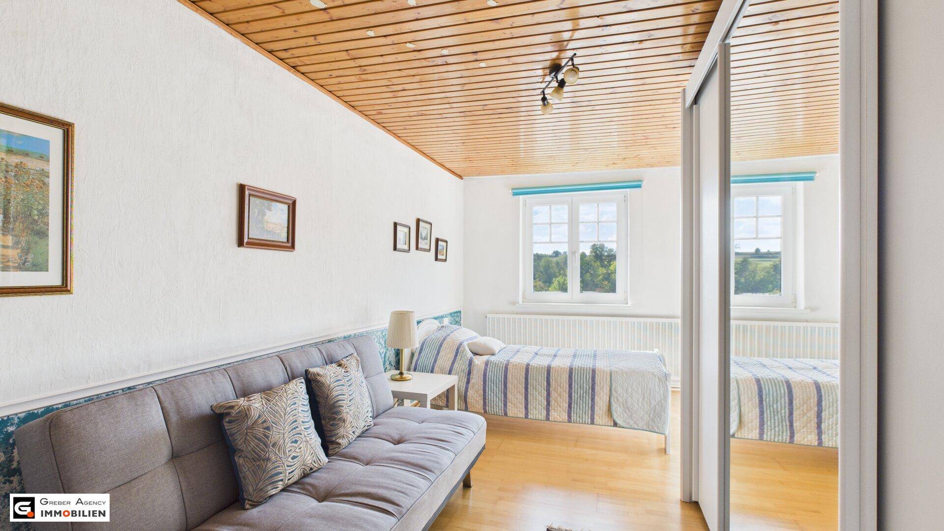 Schlafzimmer mit Holzbalkendecke, Einzelbett und Sofa, hell und freundlich.
