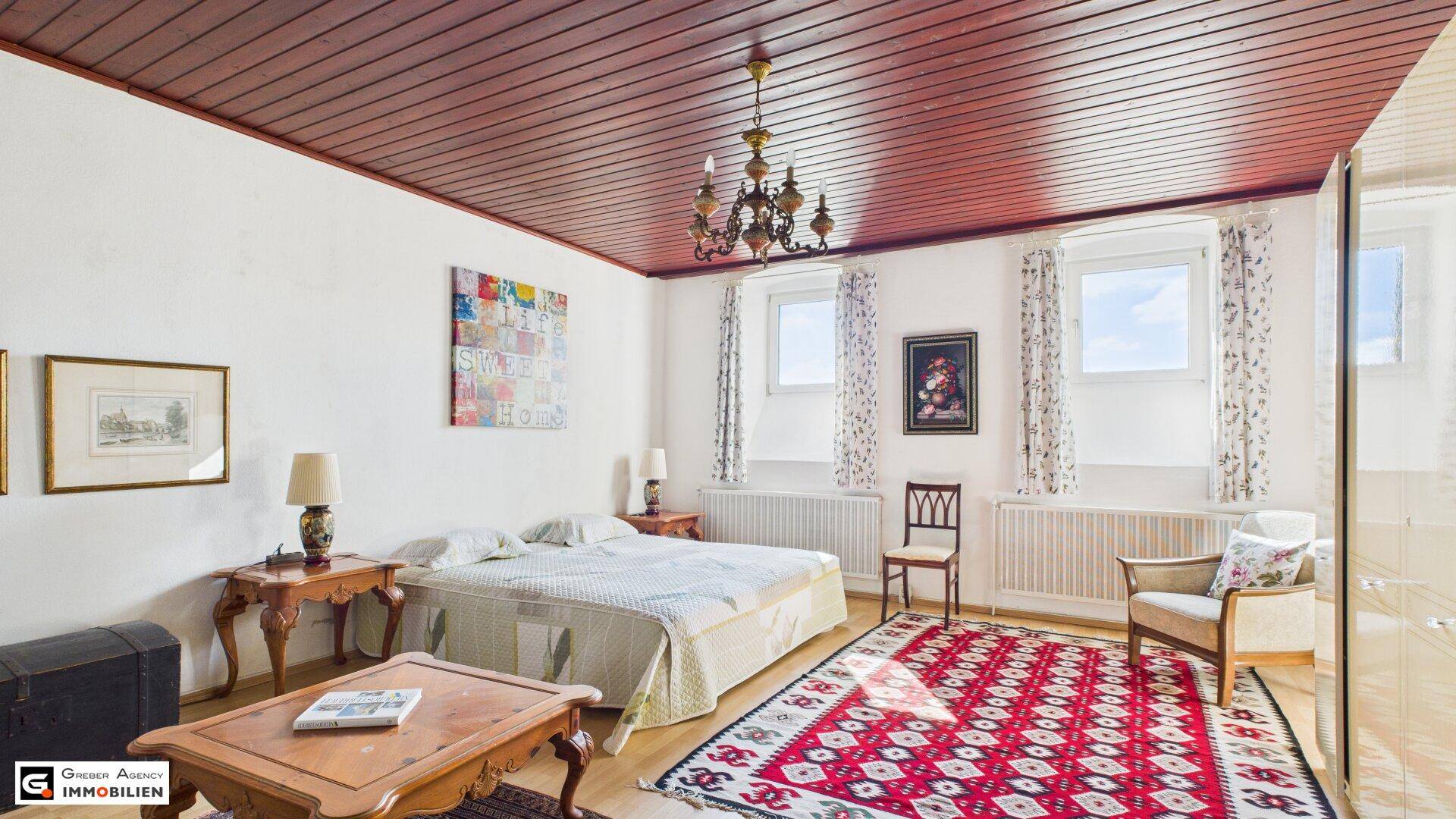 Geräumiges Schlafzimmer mit Holzbalkendecke, Doppelbett und traditionellem Teppich.