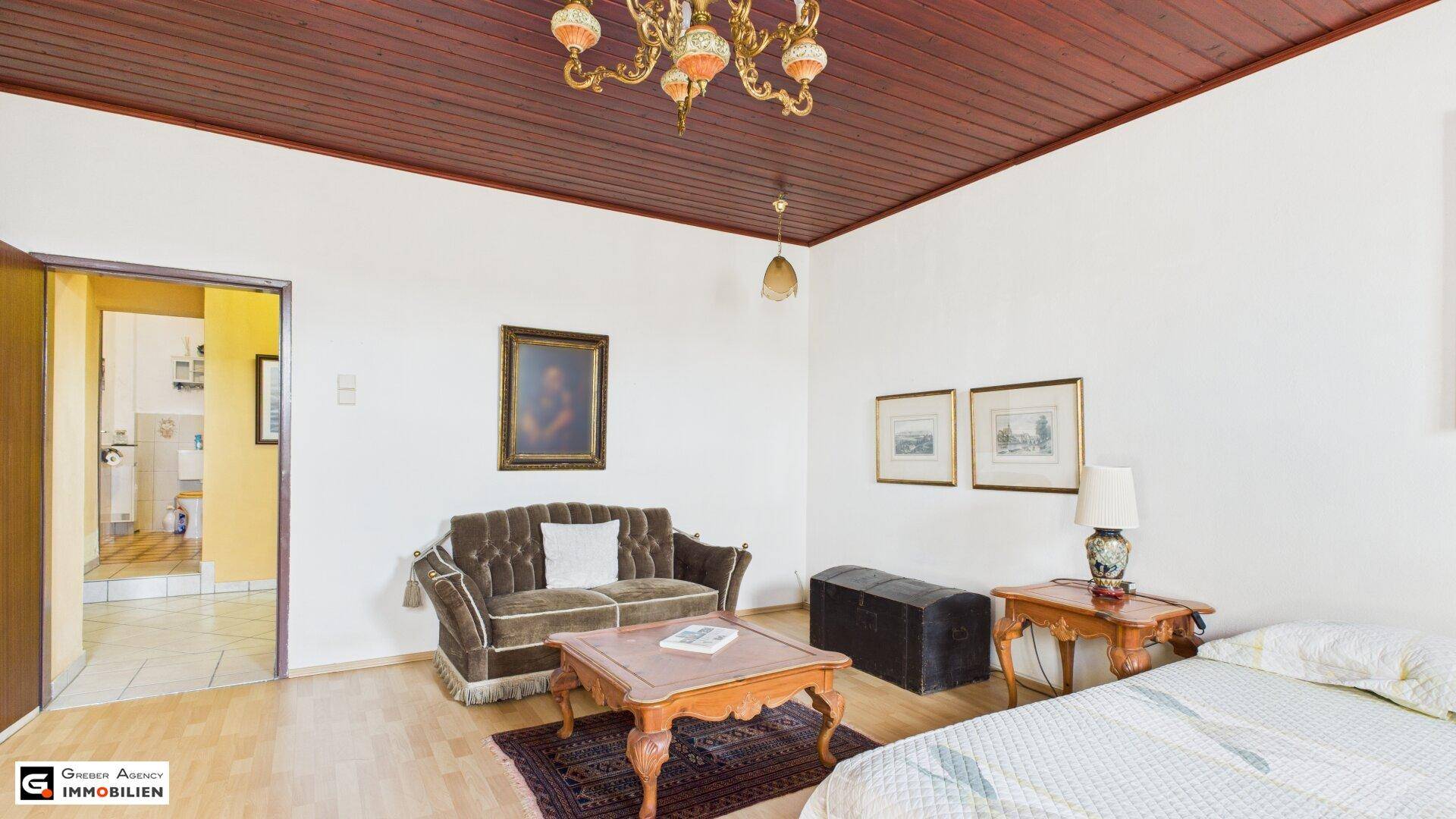 Schlafzimmer mit Holzbalkendecke, Sofa und Zugang zu einem weiteren Raum.