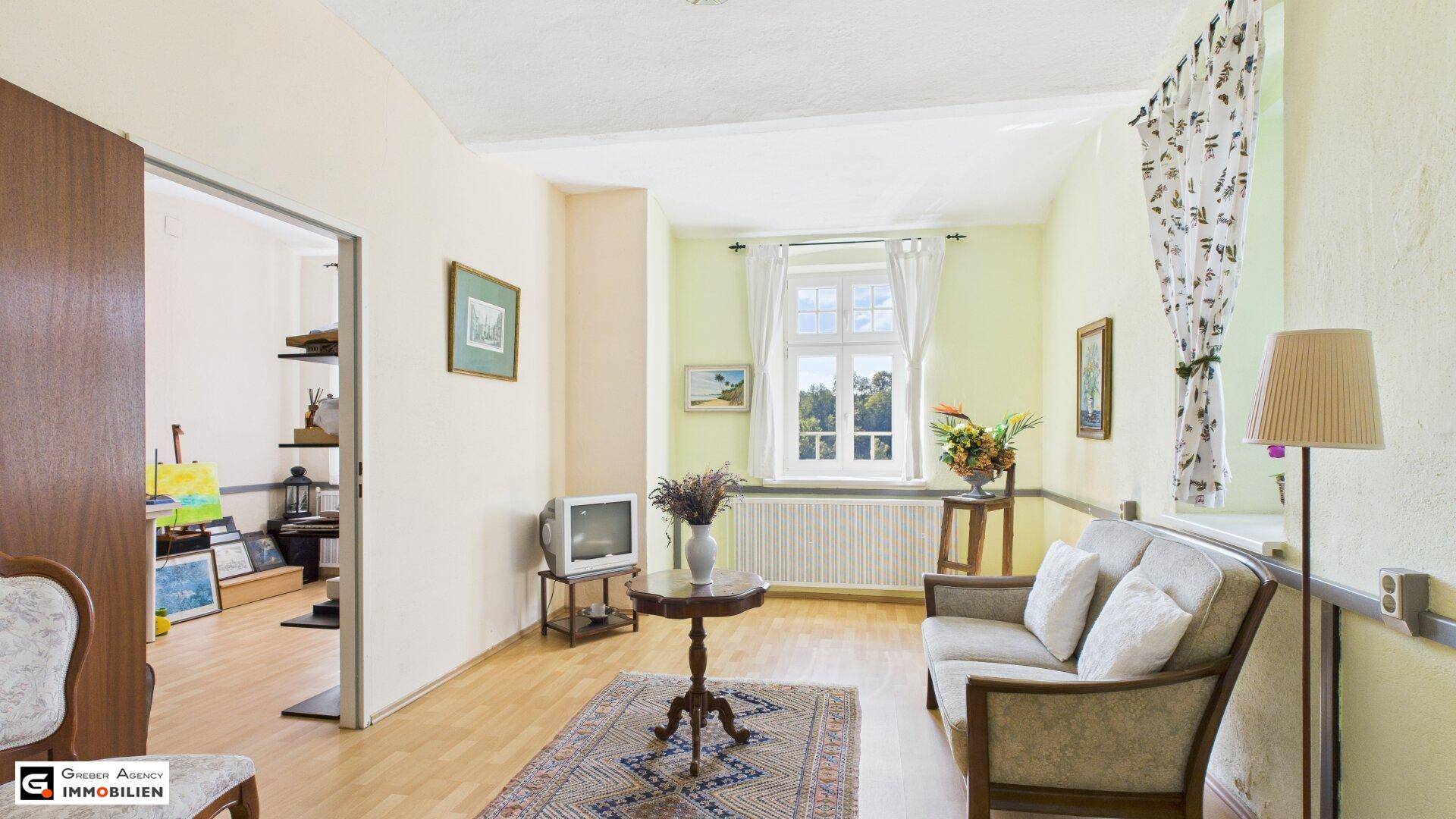 Helles Wohnzimmer mit Parkettboden, Vintage-Möbeln und Blick ins Grüne.